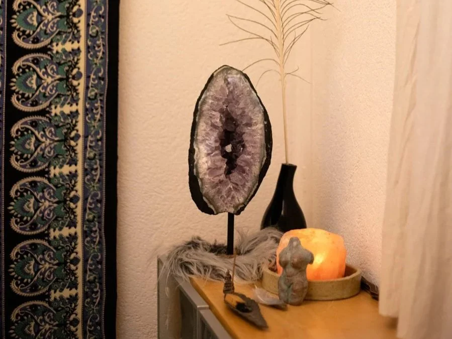 Ein Wohnzimmertisch mit einem dekorativen Kristall-Stein, einer Kerze, einer kleinen Figur, einer schwarzen Vase mit Trockenpflanze und weiteren Dekorationsgegenständen.