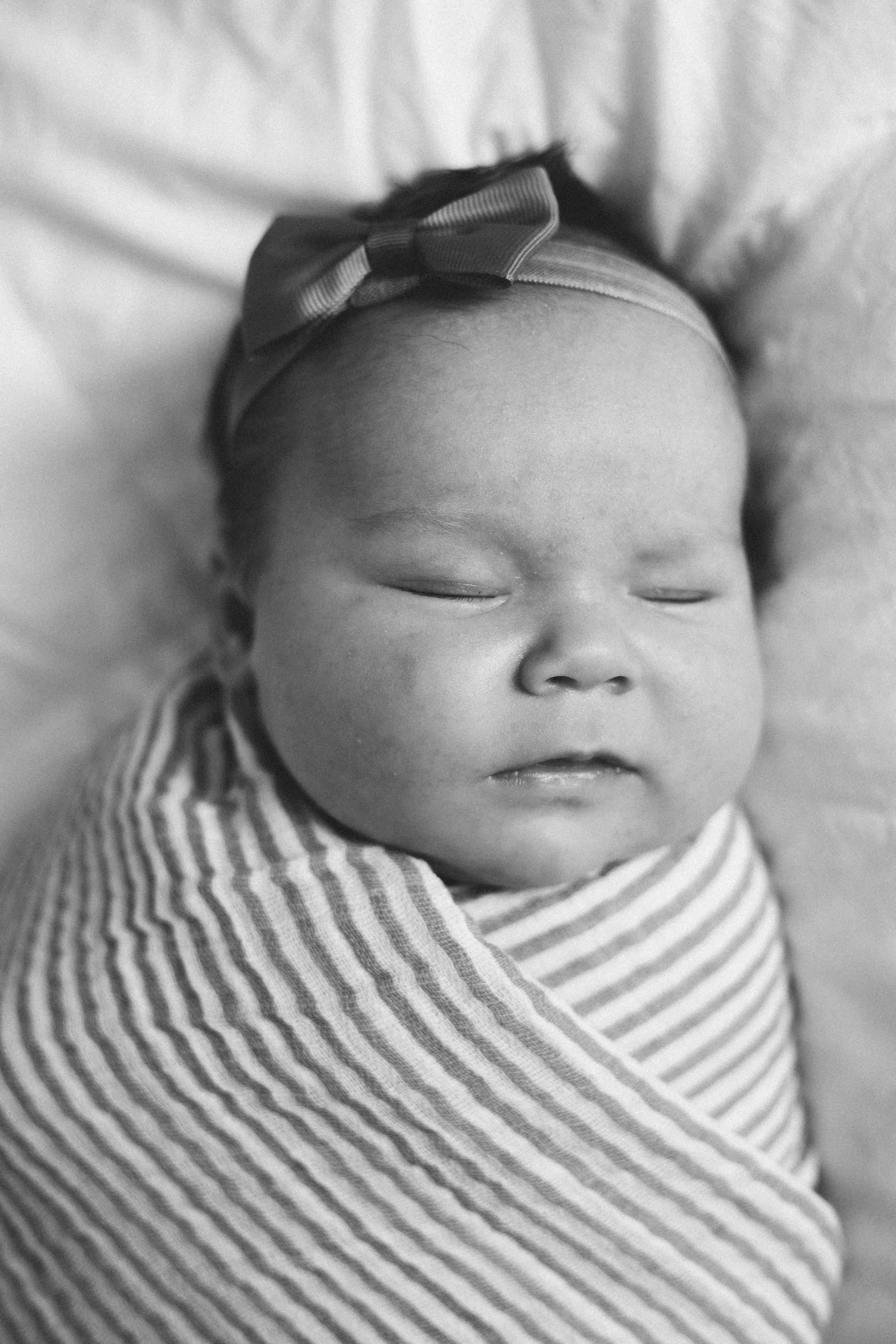Close-up of a sleeping baby with a striped outfit and a bow headband.