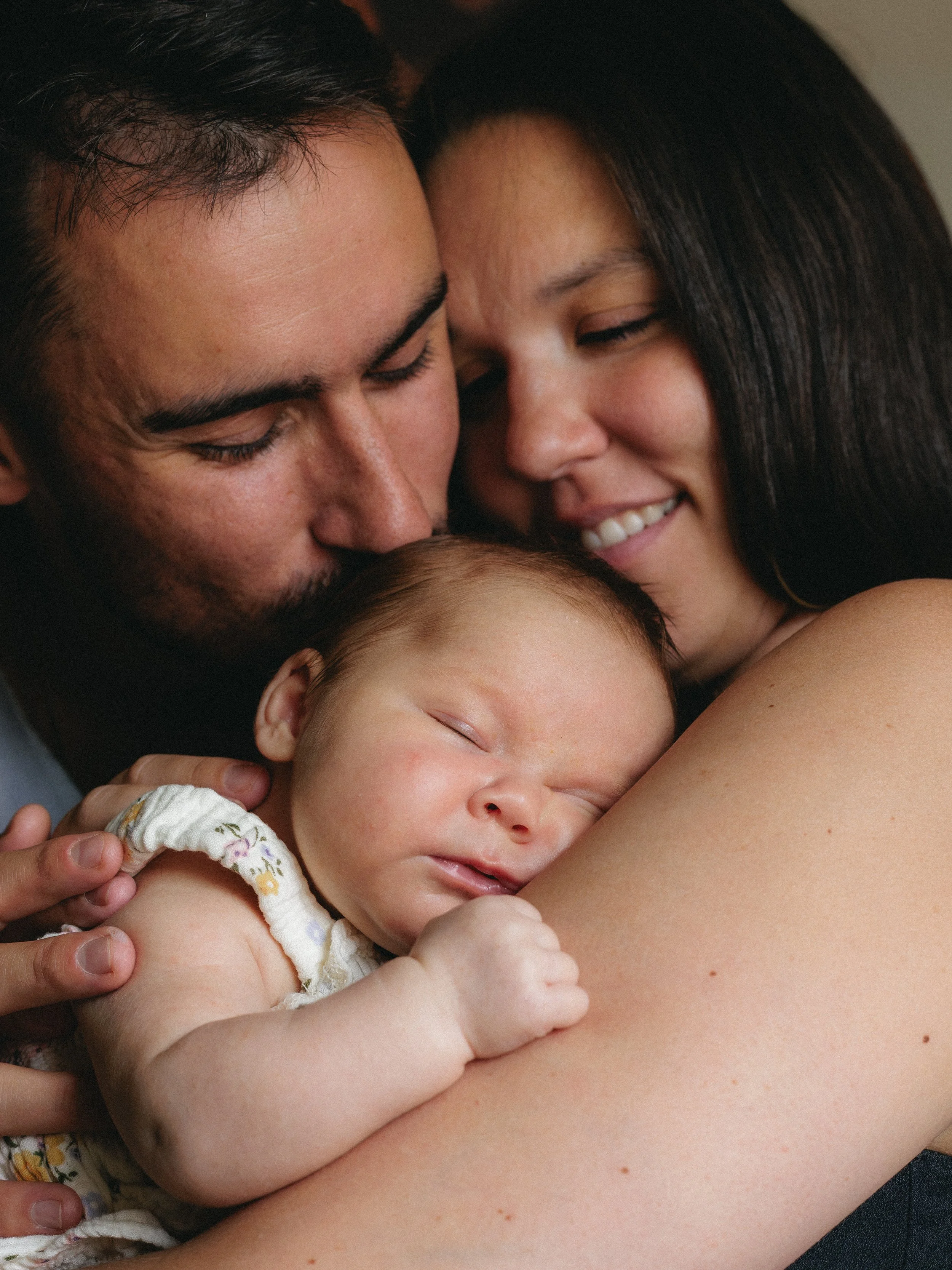 A family embracing, with a man and woman holding a sleeping baby close.