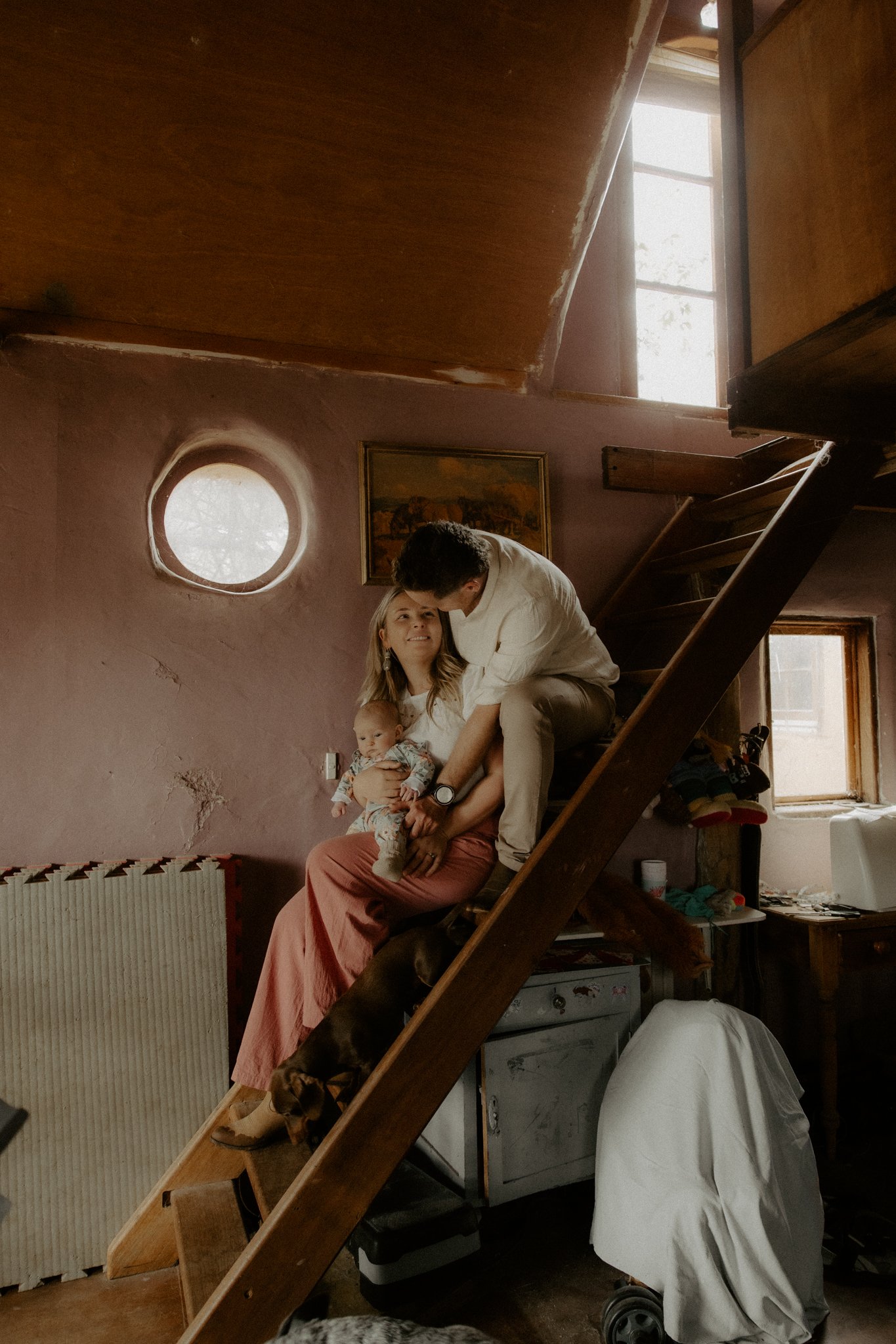 Family of three on a staircase in a cozy home, with a dog and a dog-themed sock monkey in the background.
