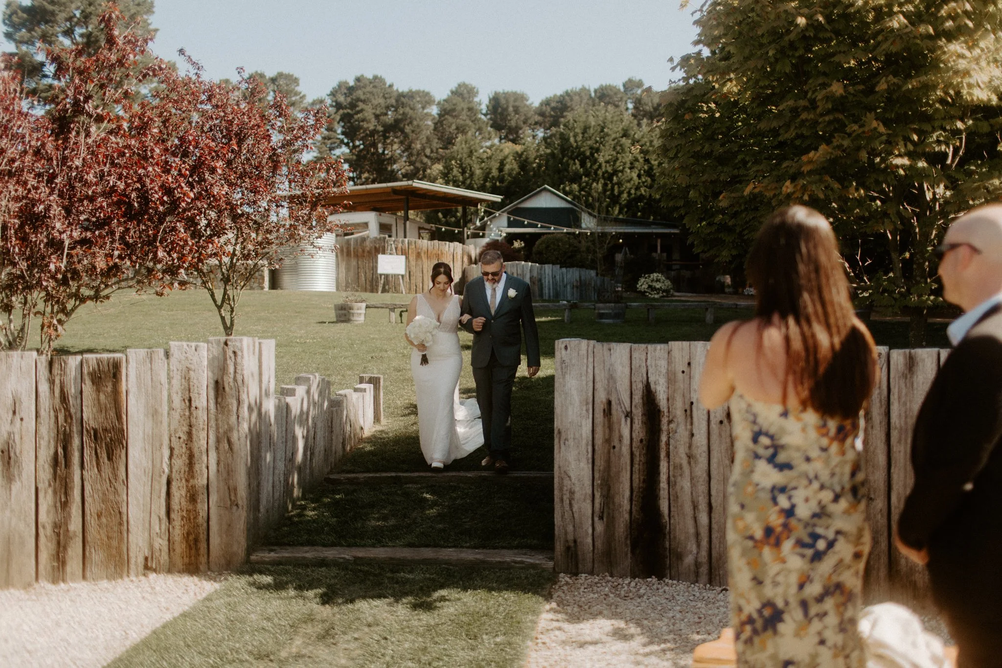 Bride entering outdoor wedding ceremony with father while guests watch at Seclusions Blue Mountains.