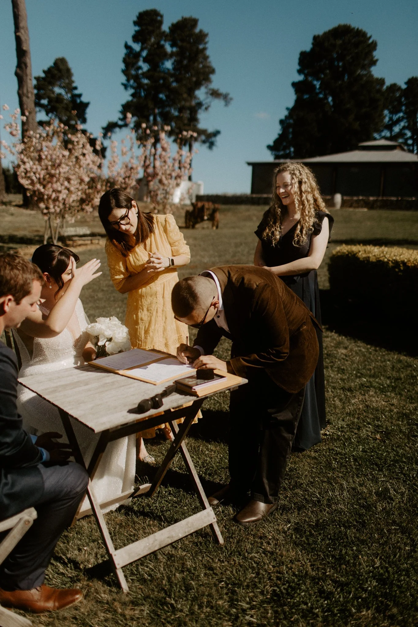 People at an outdoor wedding signing documents, with some smiling and talking during a Blue Mountains wedding at Seclusions Blue Mountains.