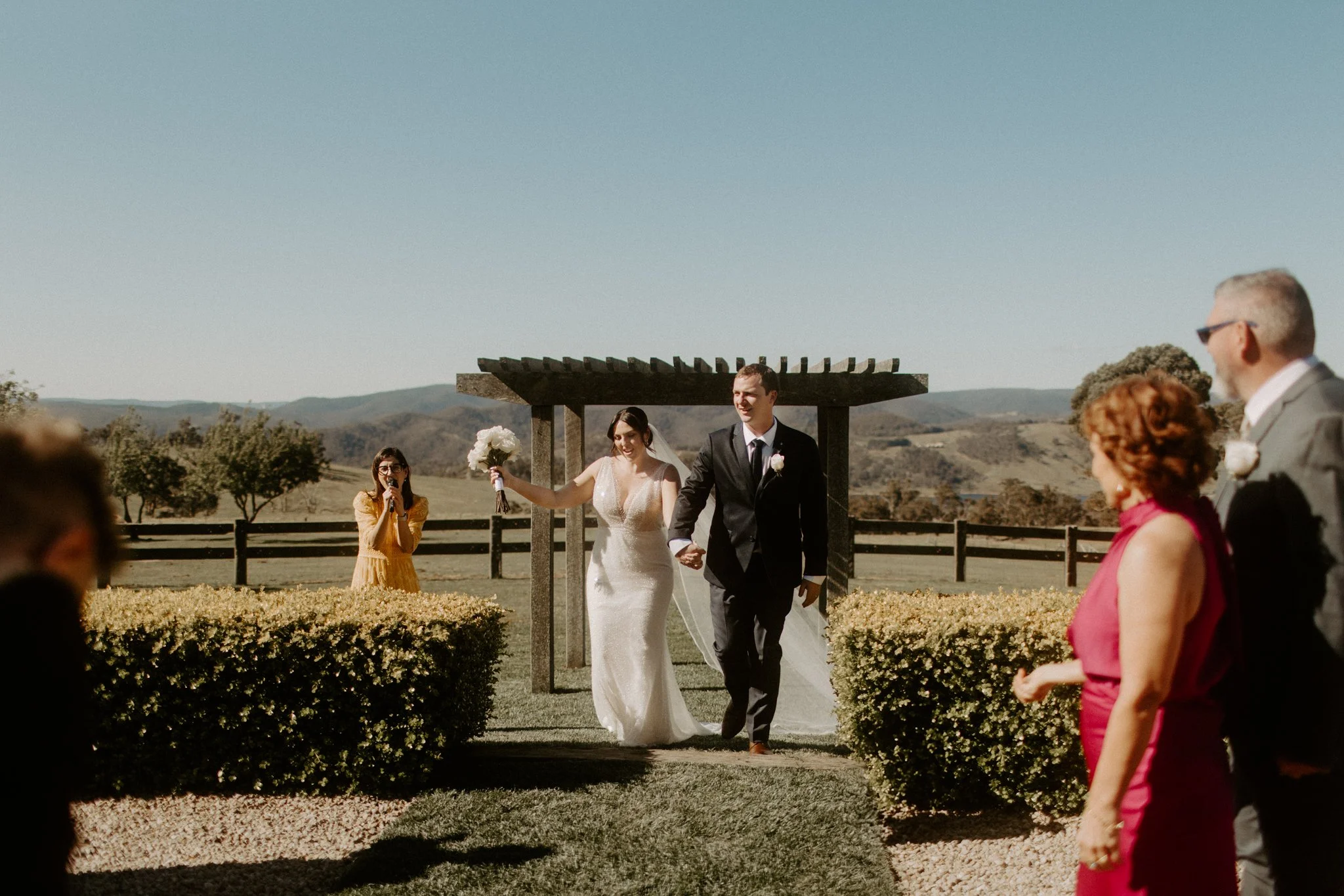 A bride and groom walking hand in hand after their wedding ceremony outdoors, with guests watching during a Blue Mountains wedding at Seclusions Blue Mountains.