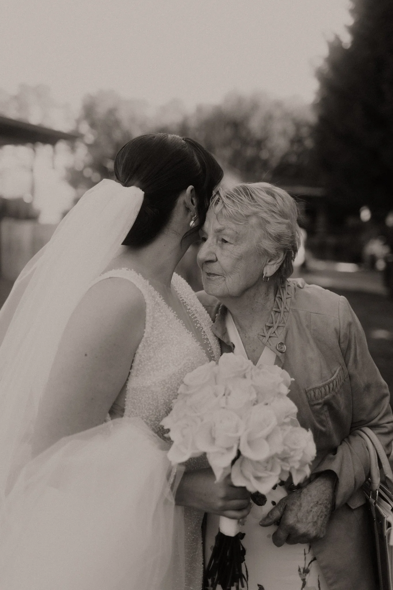 A bride and an elderly woman sharing a close moment, with the bride holding a bouquet of flowers.