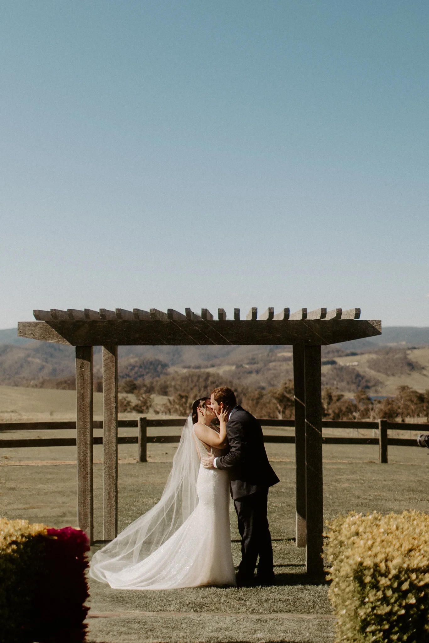 Bride and groom kissing under an outdoor wooden arbor with scenic landscape in background during a Blue Mountains wedding at Seclusions Blue Mountains.