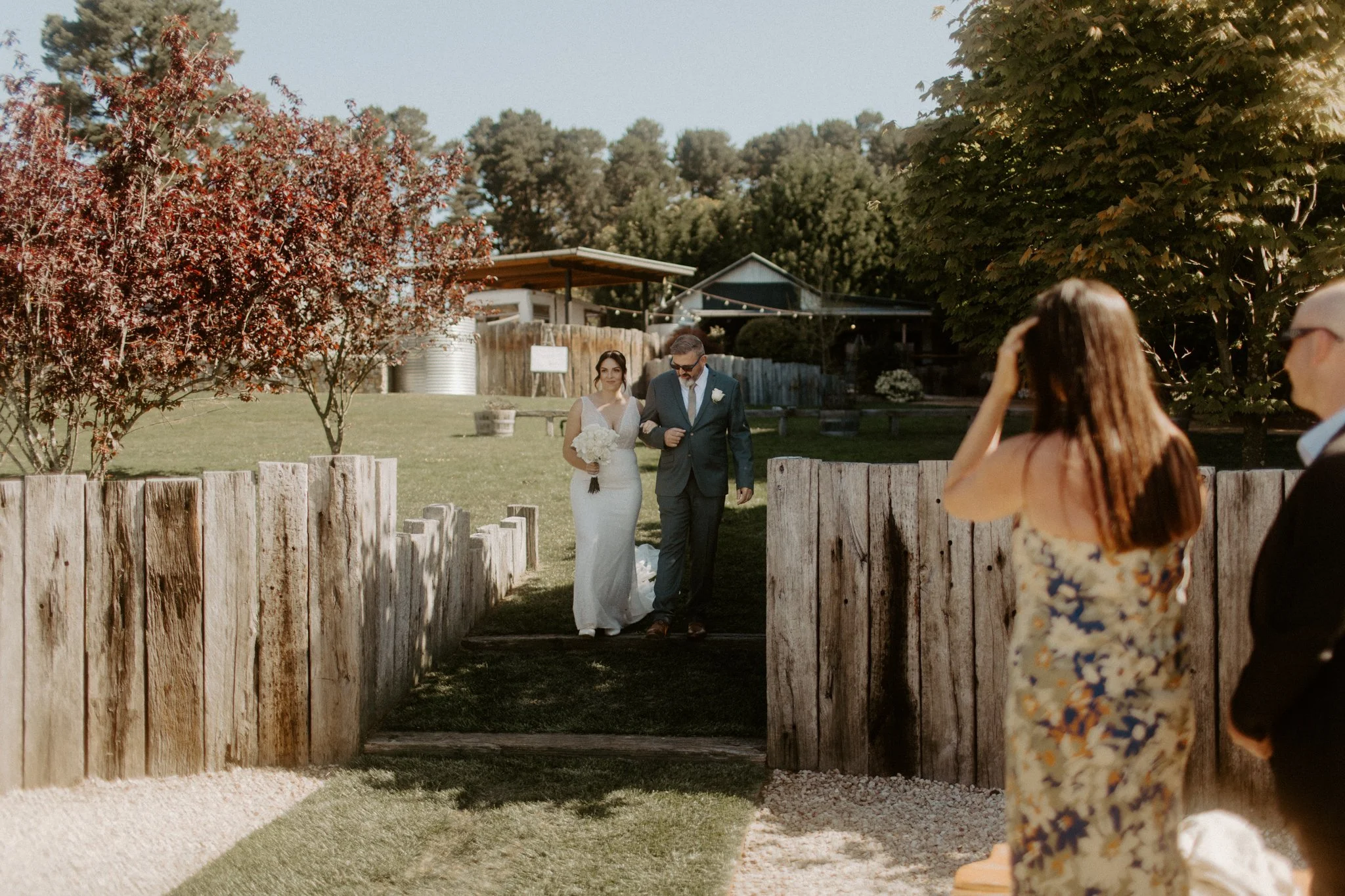 Bride entering outdoor wedding ceremony with father while guests watch at Seclusions Blue Mountains.