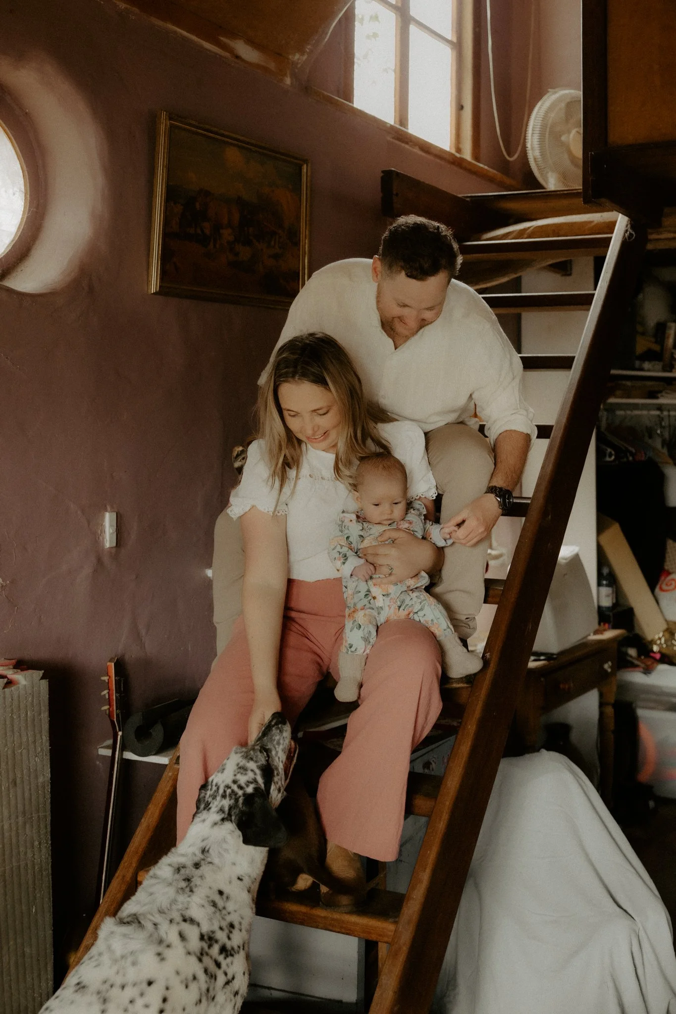 A family standing on a staircase with a Dalmatian dog, a woman holding a baby, a man smiling, and the dog reaching up to the woman.