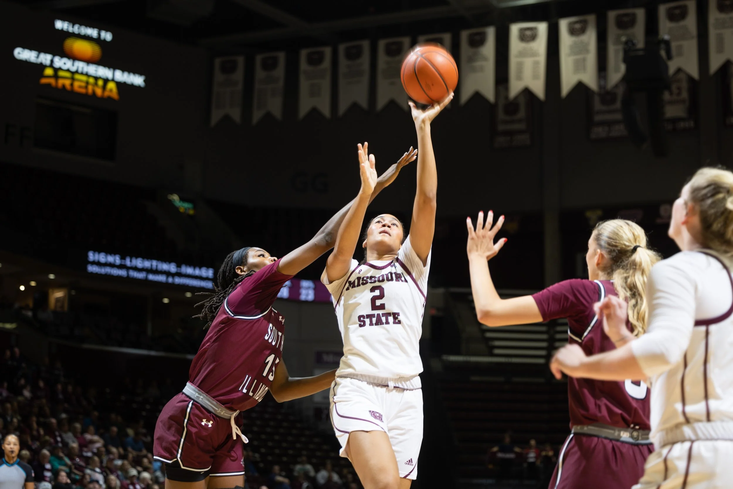 A women's basketball game with a player from Missouri State shooting a shot while being guarded by players from Southern Illinois in a sports arena.