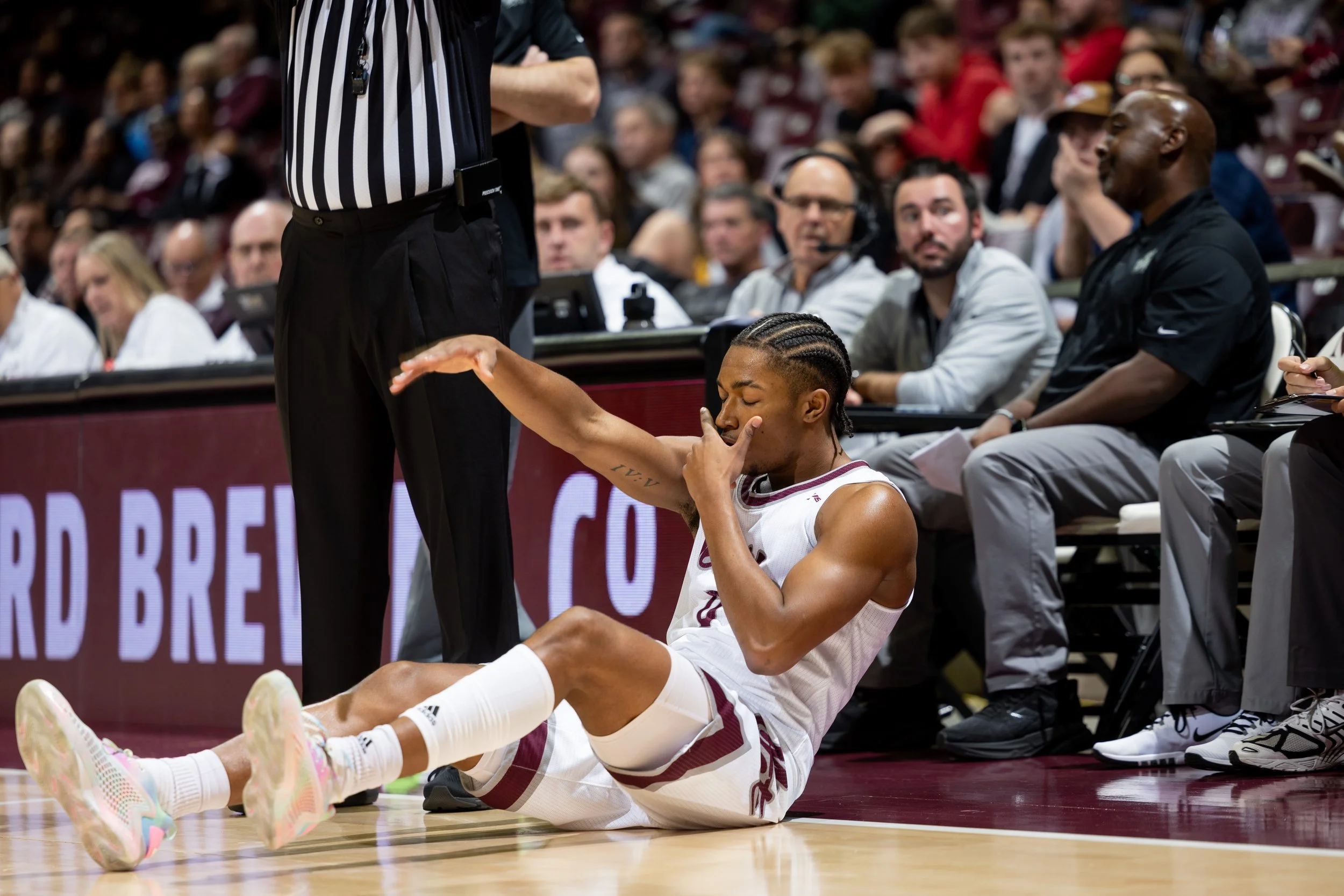 A basketball player sitting on the court holding his injured ankle, with medical staff and spectators watching.