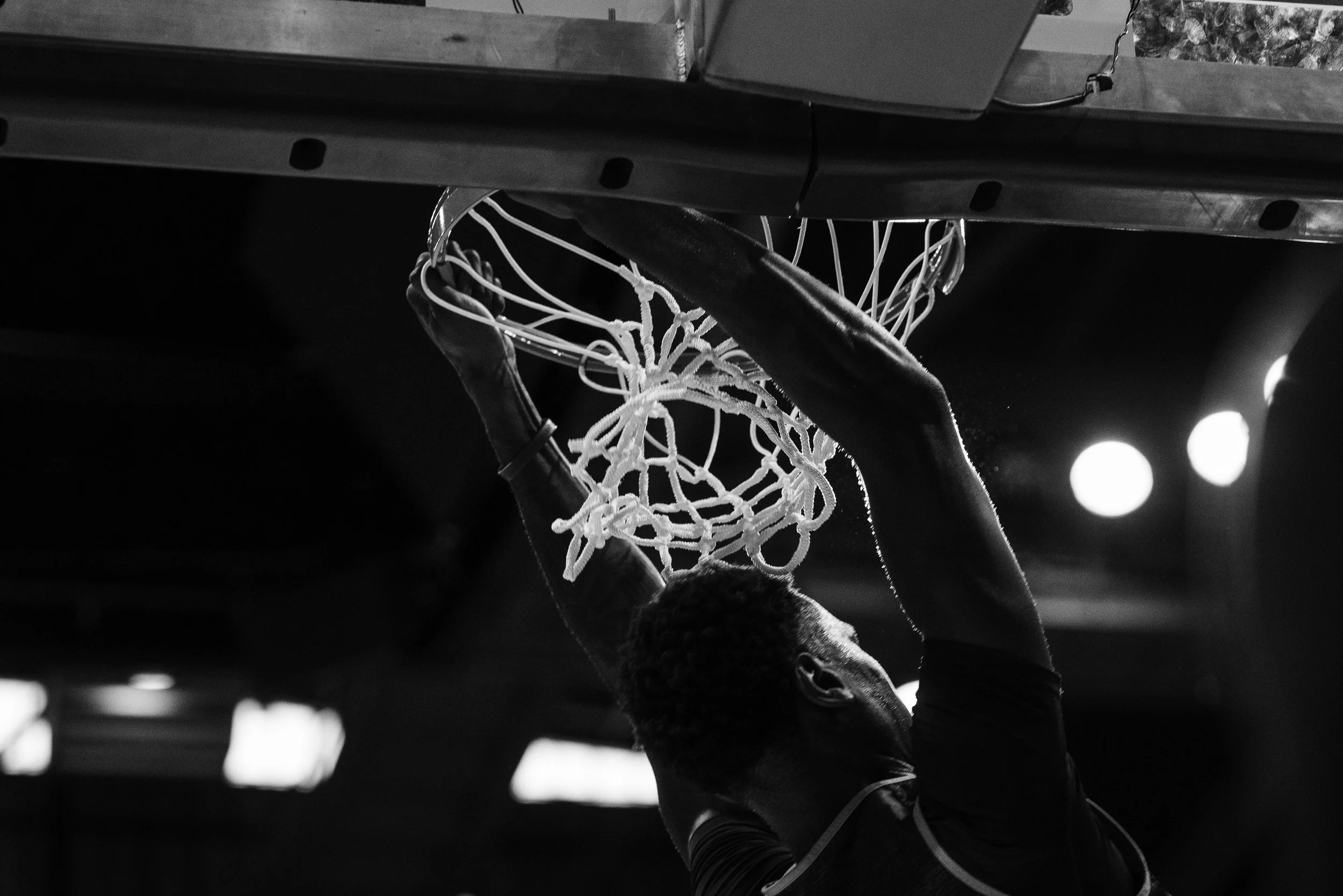 A basketball player is dunking a ball into the hoop during a game, captured from a side angle.