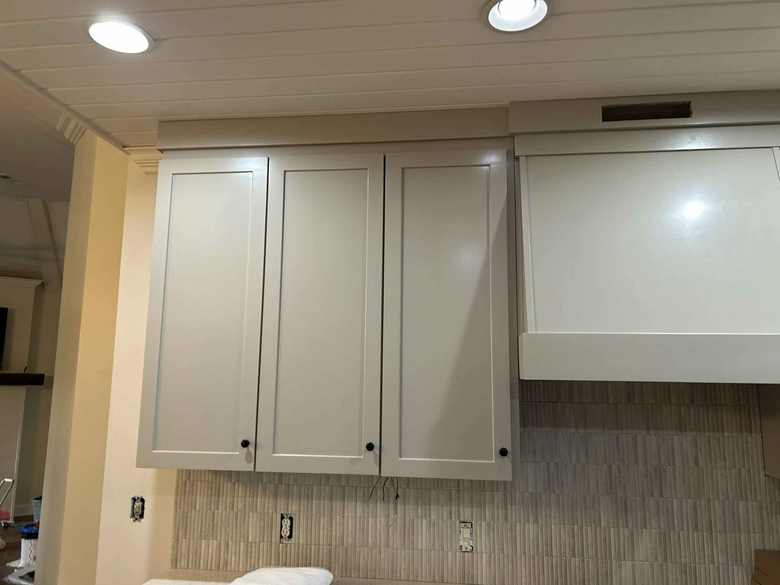 White kitchen cabinets with black knobs and a textured beige tile backsplash.