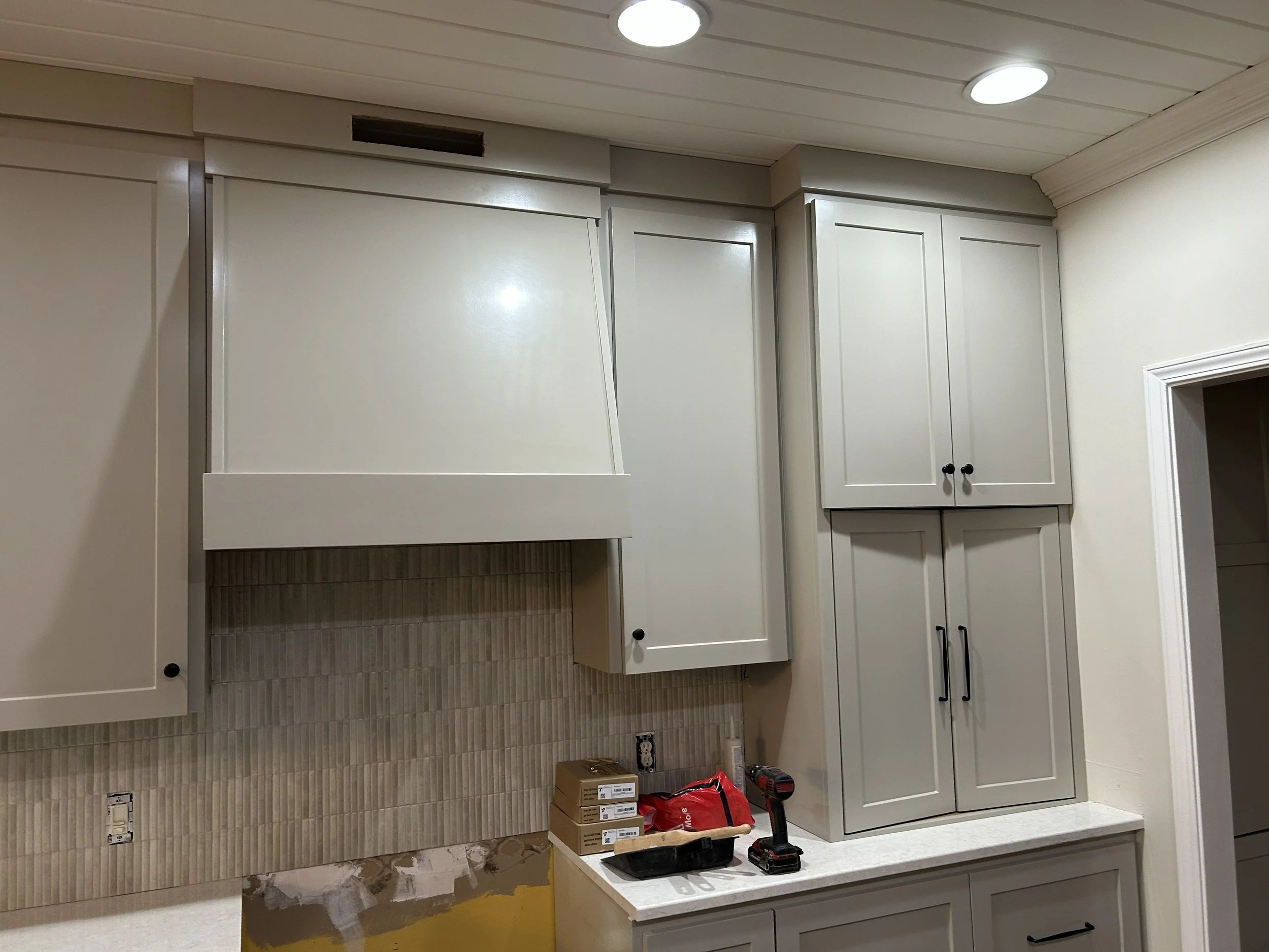 Kitchen cabinets being installed with tools and materials on the counter, beige tiled backsplash, and unfinished wall area.