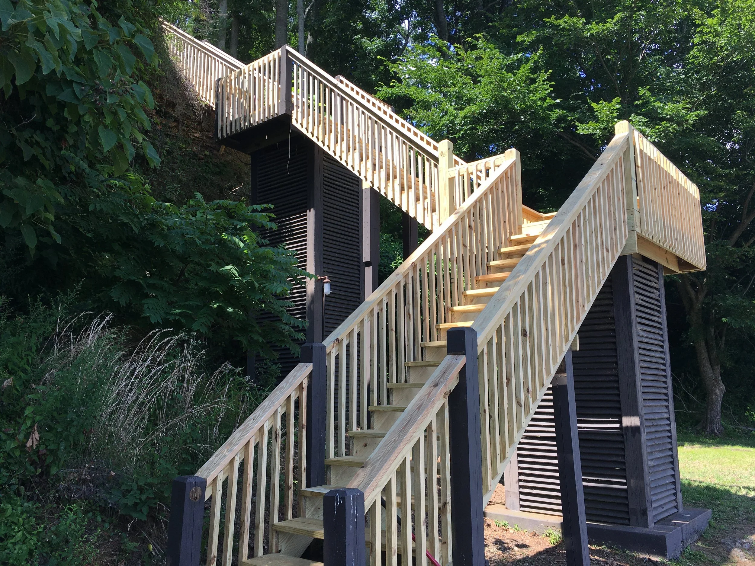 Construction of a new wooden staircase leading up to an elevated platform, with trees and greenery in the background.