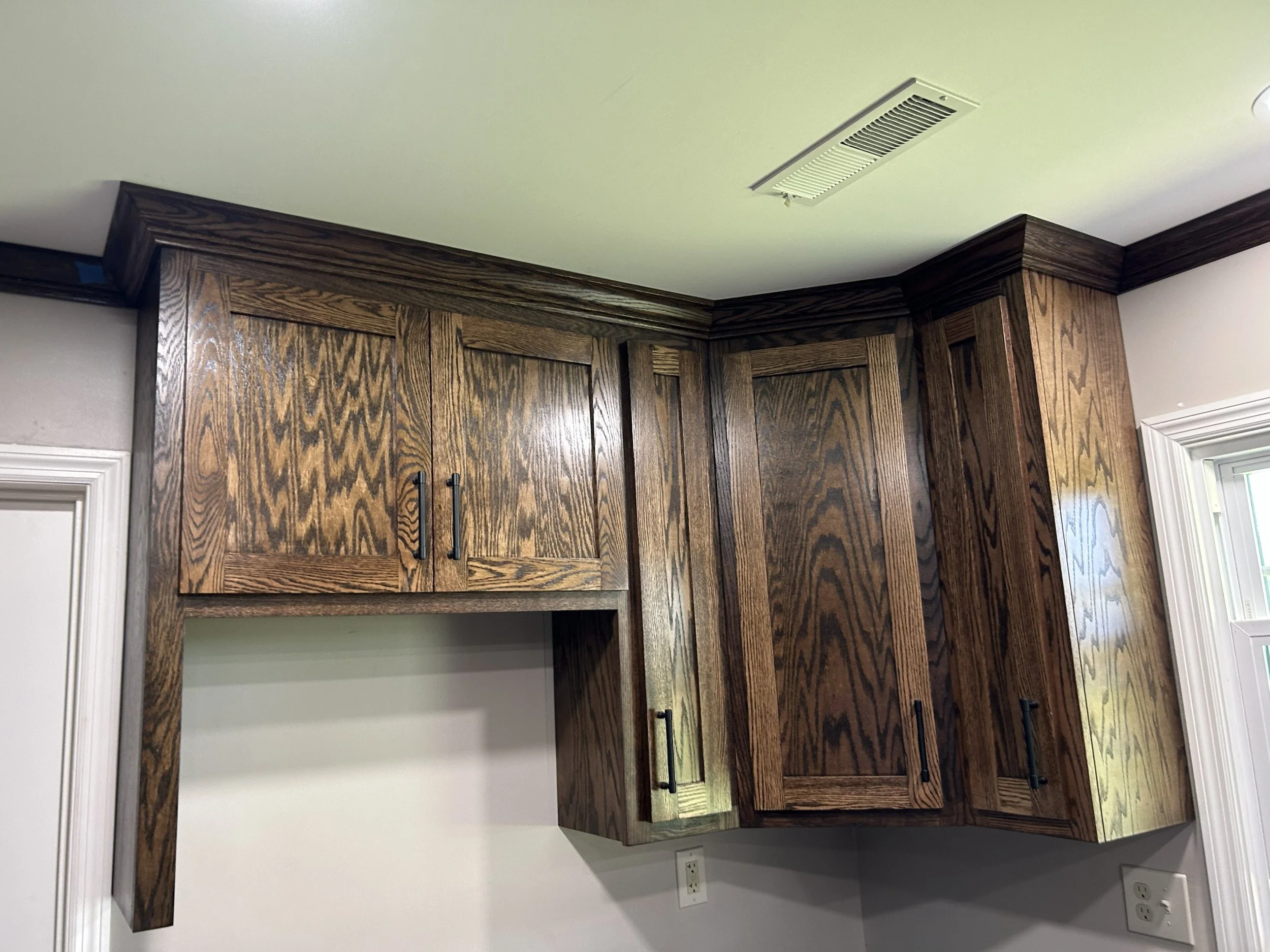 Kitchen upper cabinets made of dark wood with black handles, white wall, and an electrical outlet below