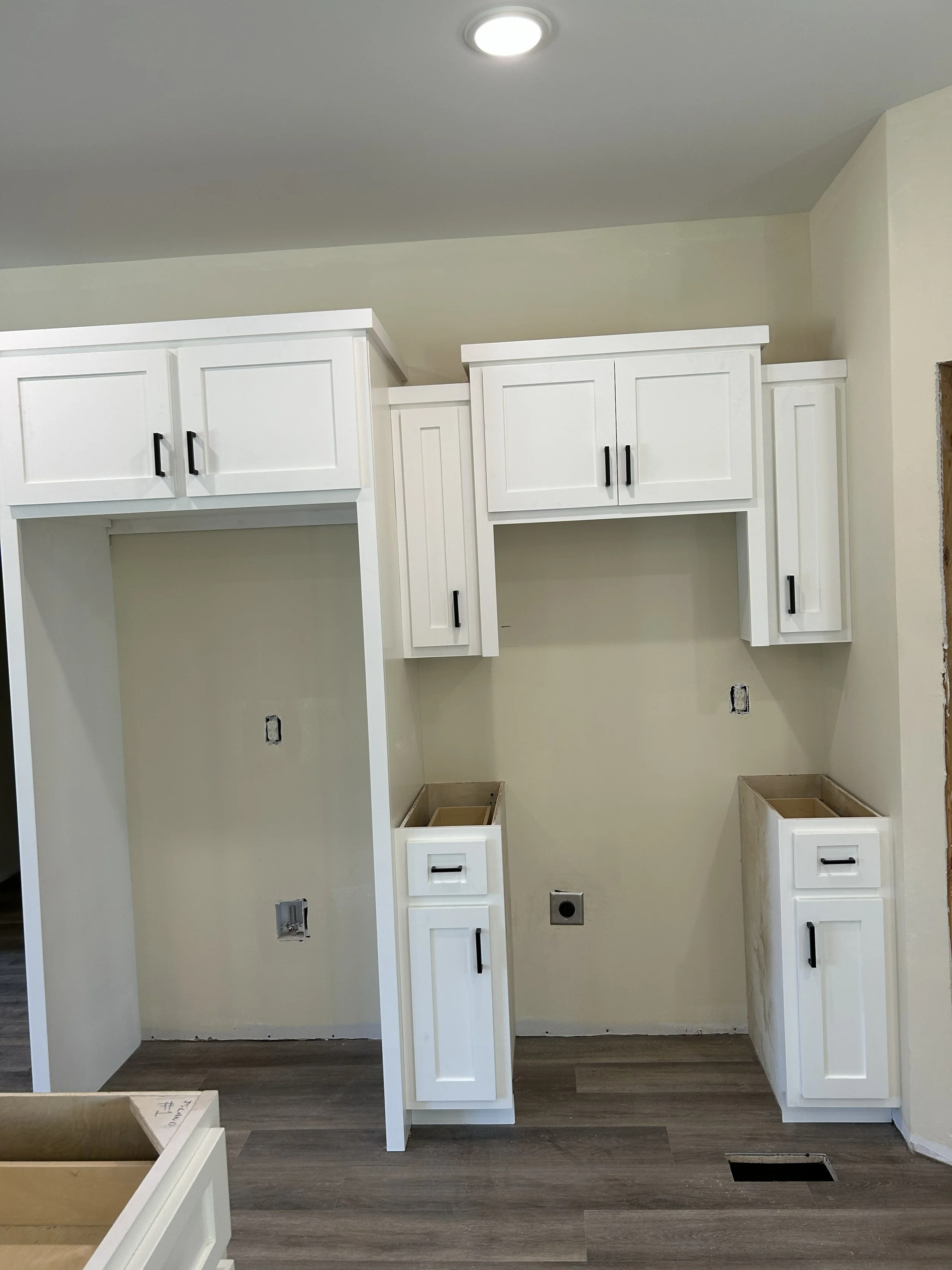 Kitchen cabinet project in progress with white cabinets, some open spaces for appliances, and no countertops installed yet.