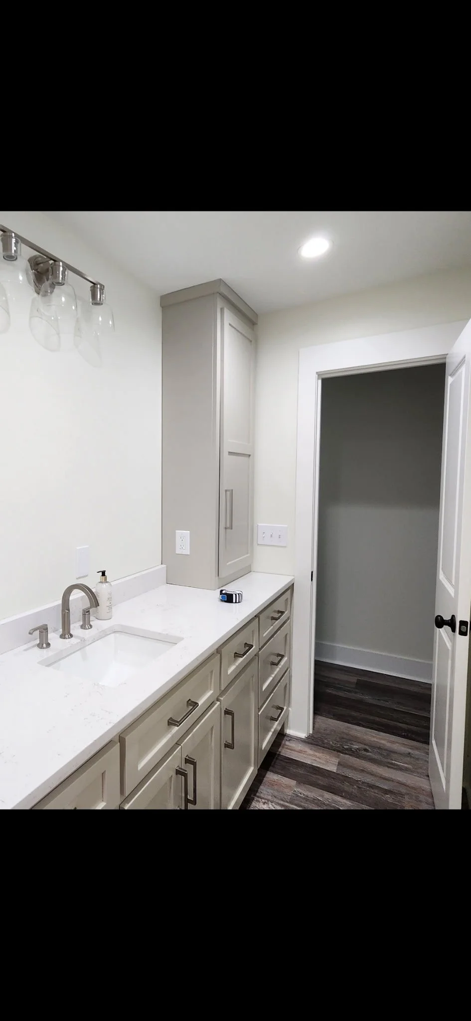 Modern bathroom with white cabinetry, a white countertop, a small sink, silver handles, a mirror above the sink, and dark wood flooring.