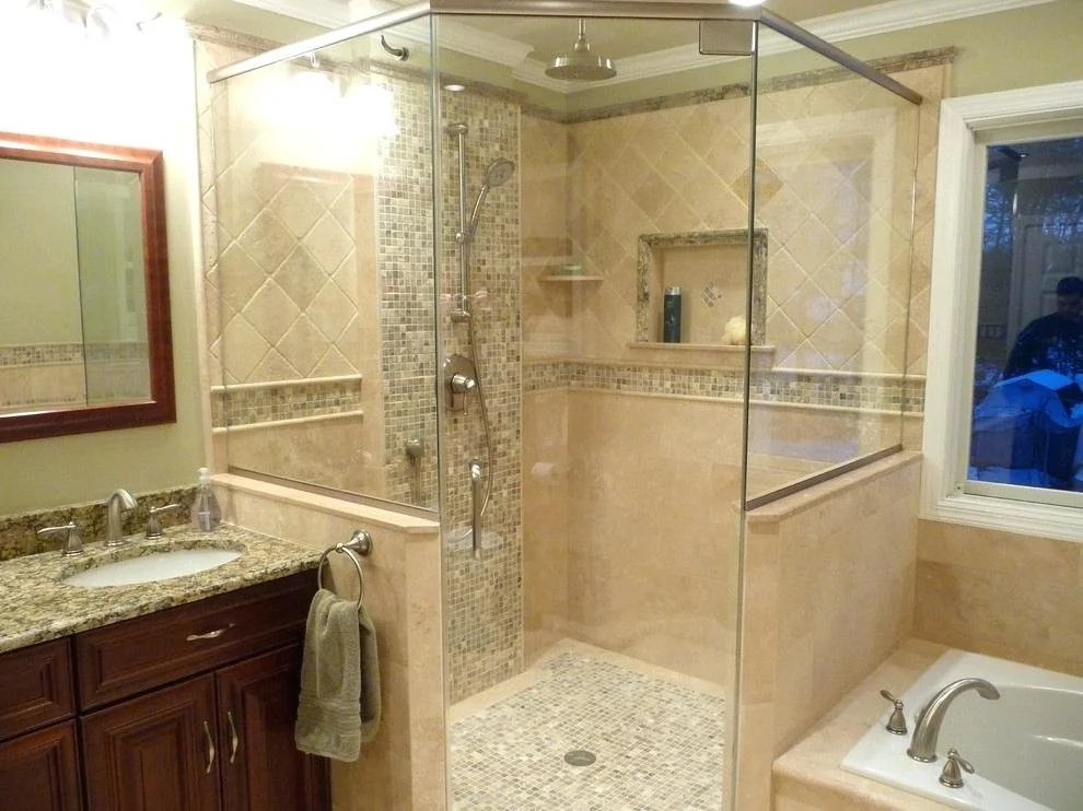 Bathroom with a granite countertop vanity, a towel ring with a towel, a large mirror, a glass-enclosed shower with beige and mosaic tile walls, a built-in shelf, a window, and a corner bathtub.