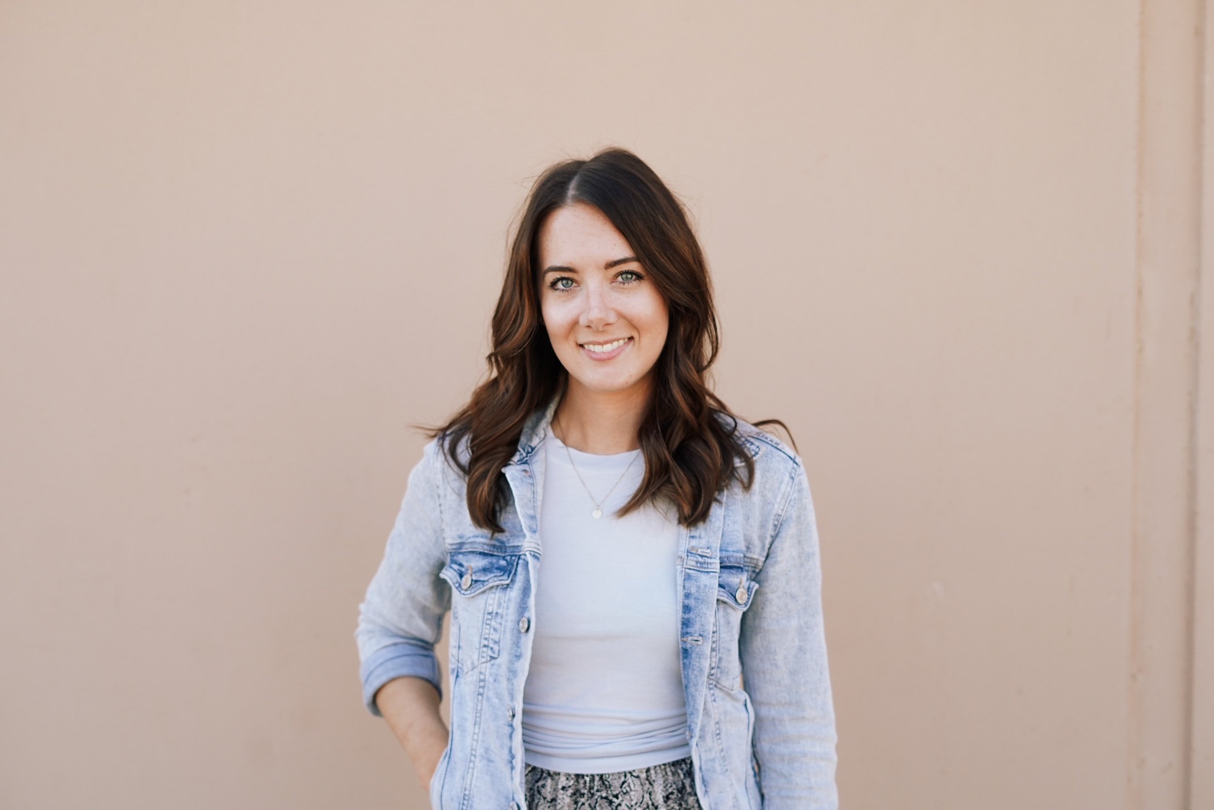 artist Tess Ciarloni standing against a pink wall with a jean jacket