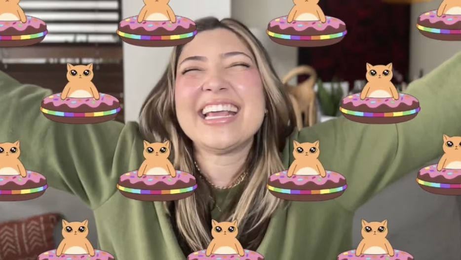 A woman with blond hair and a green shirt smiling with her arms raised, surrounded by animated donuts with pink frosting and sprinkles, and cartoon cats sitting on top of the donuts.