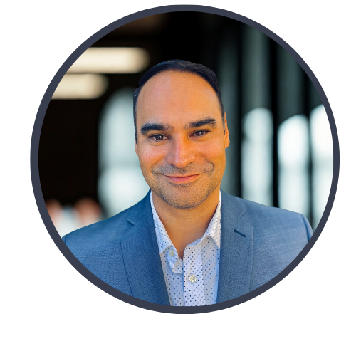 Portrait of a man in a blue blazer and white shirt smiling, with a blurred indoor background and circular frame.