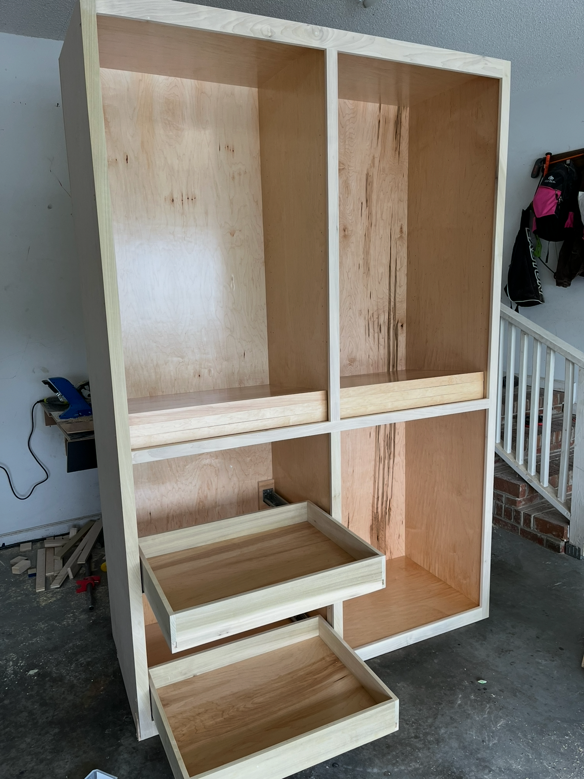 Wooden shelving unit with four large compartments, two open drawers at the bottom, in a garage or workshop space.