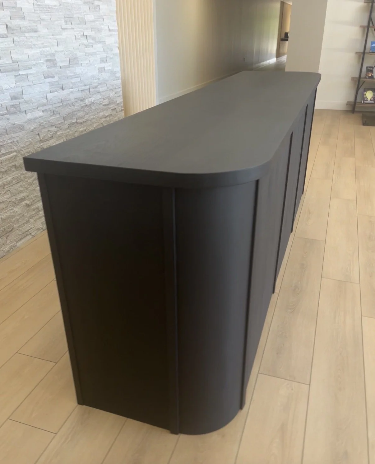Dark-colored cabinet with a curved front, placed on a light wood floor in a modern interior space.