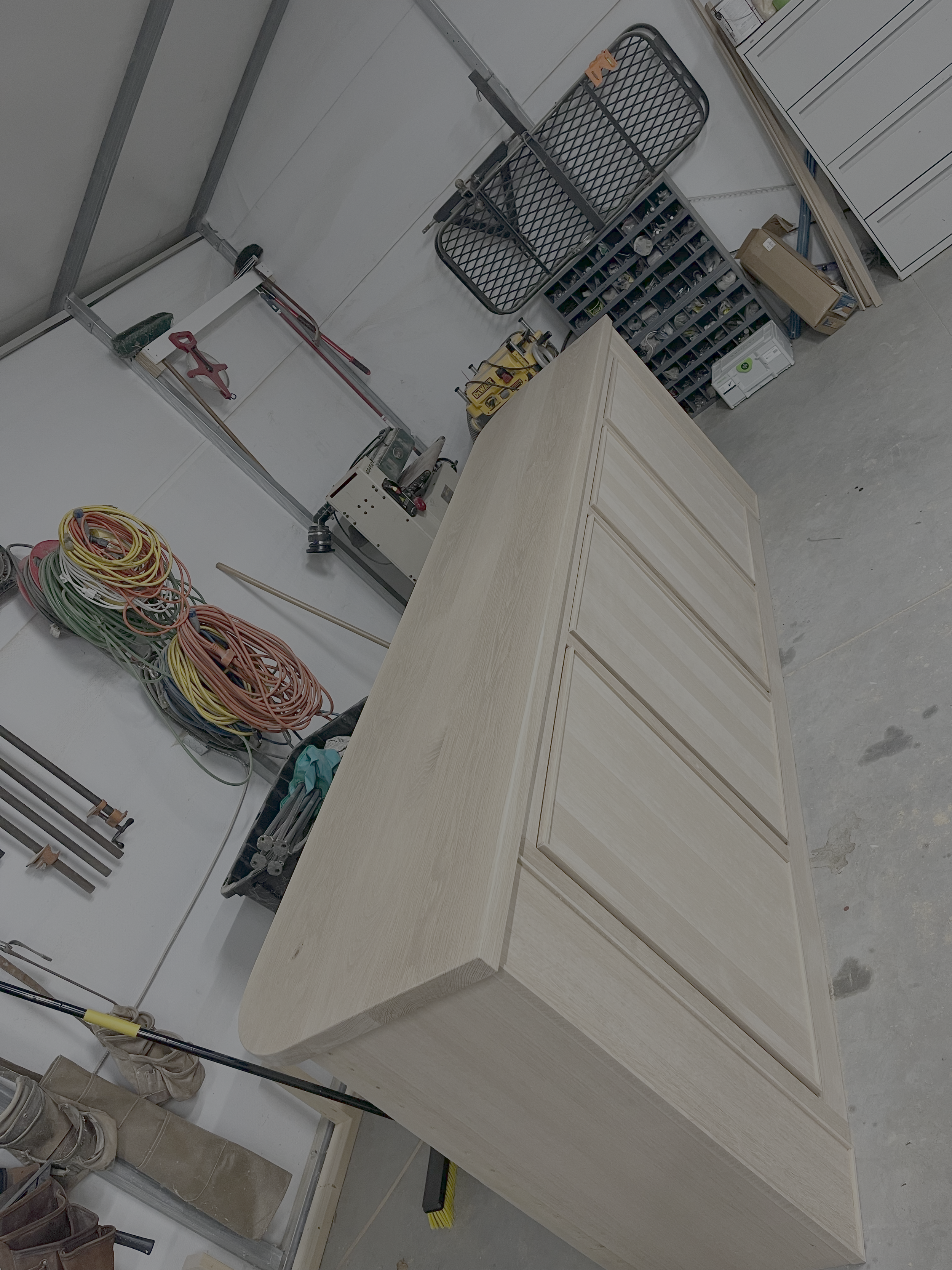 A woodworking workshop with a partially assembled wooden cabinet, tools, and supplies on workbenches and shelves.