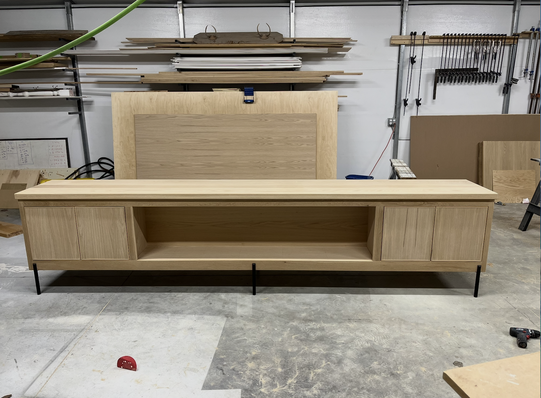 unfinished wooden media console with cabinets and open shelf in woodworking workshop.