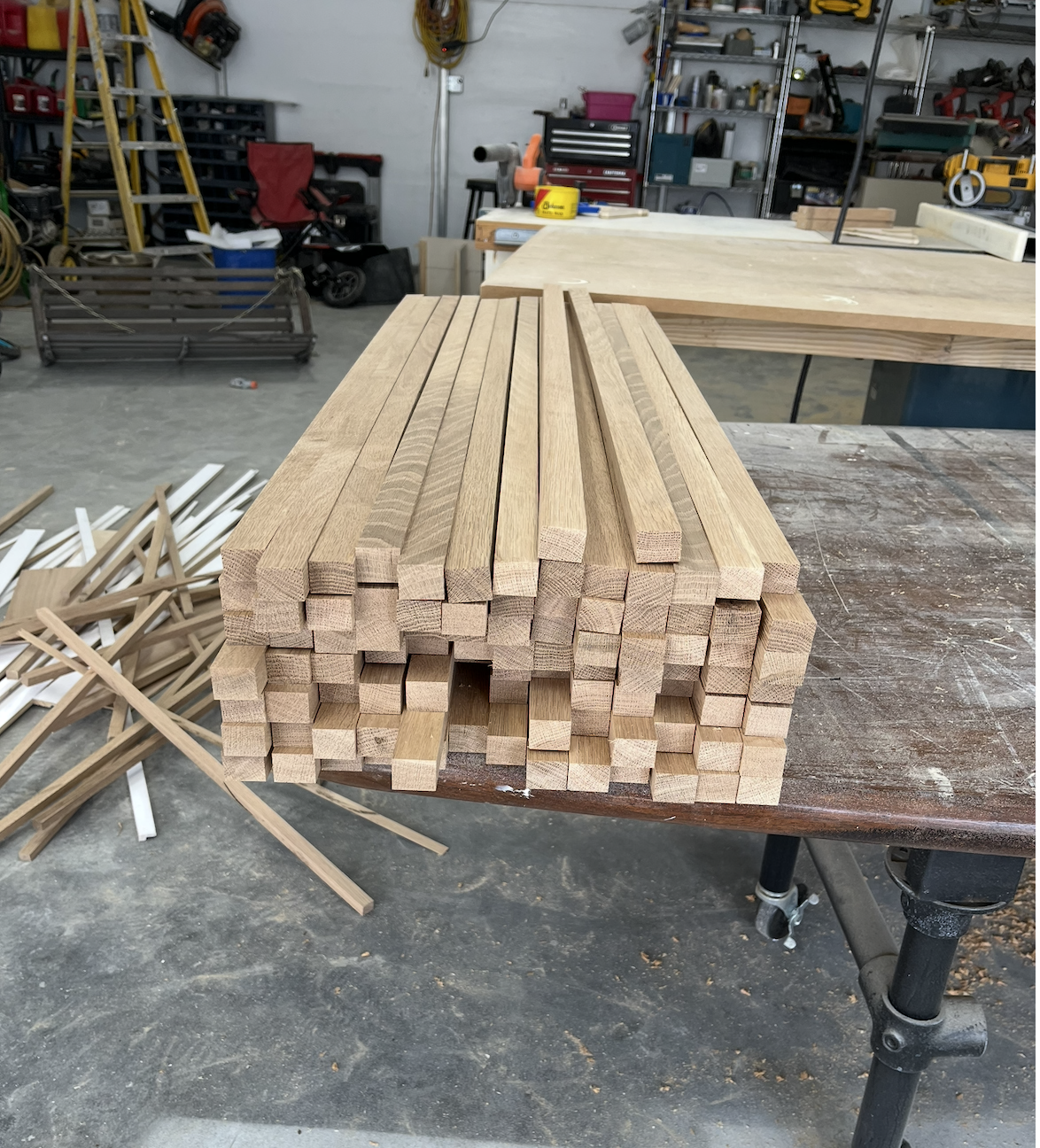 Stacked wooden planks on a workbench in a woodworking shop, with various tools and supplies in the background.
