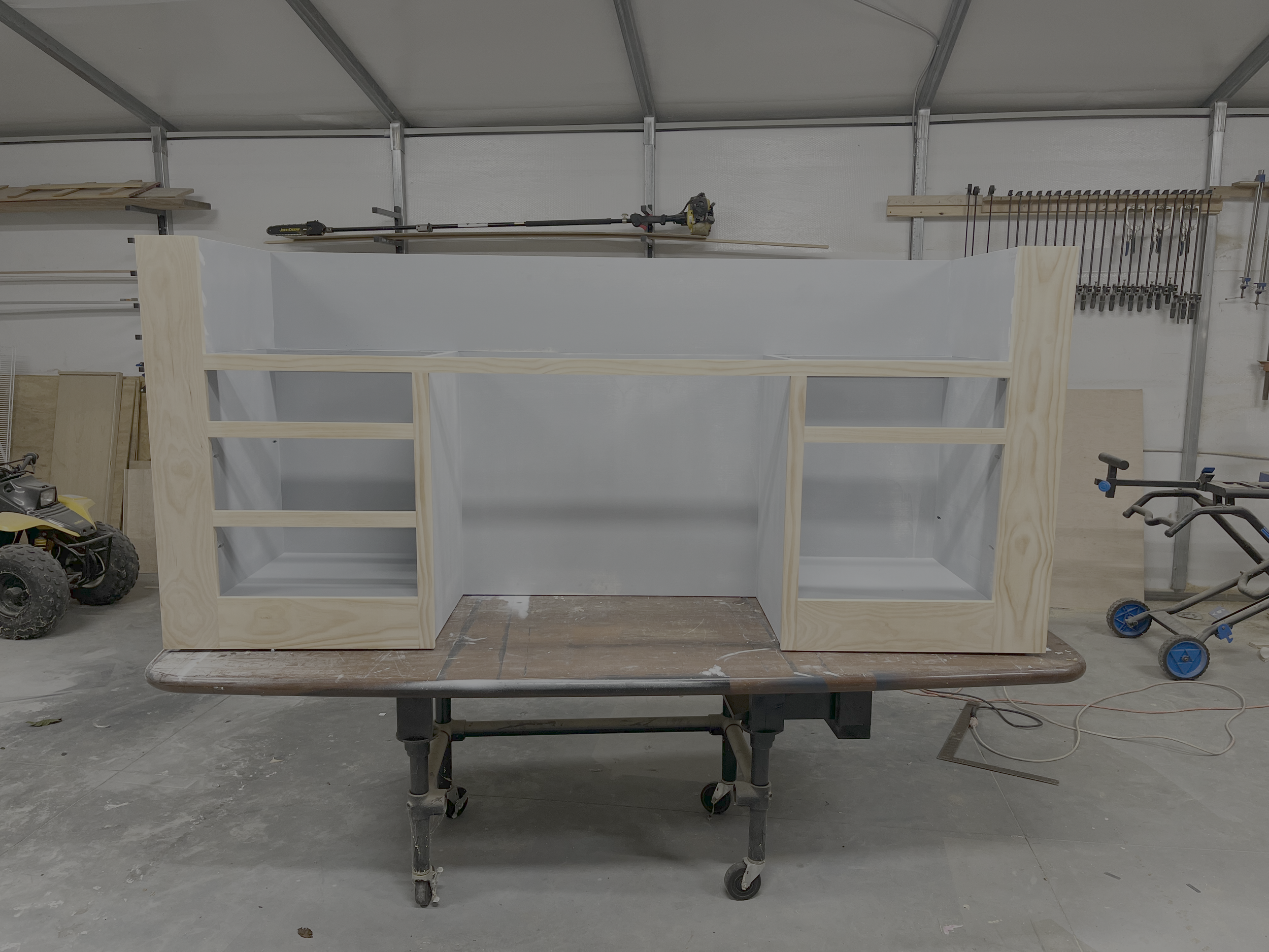 Wooden workbench with a partially built cabinet or shelving unit on top, in a woodworking shop.