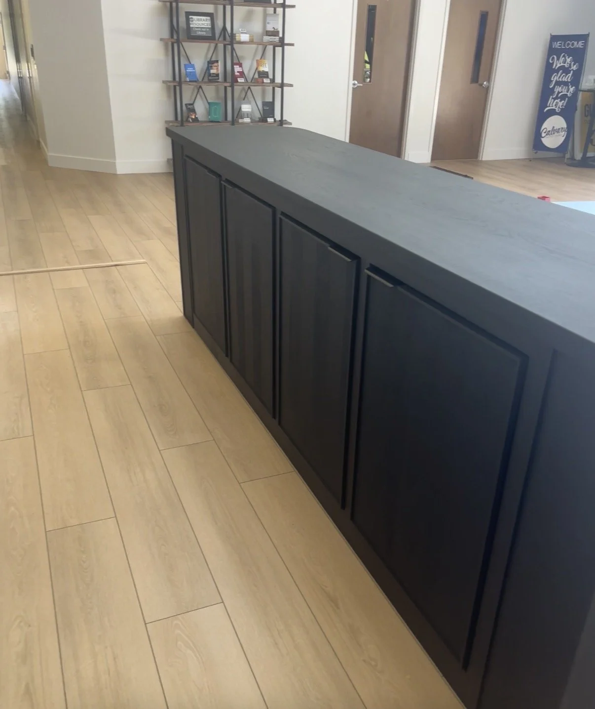 A black countertop and cabinets inside a room, with a bookshelf and signs on the wall in the background.