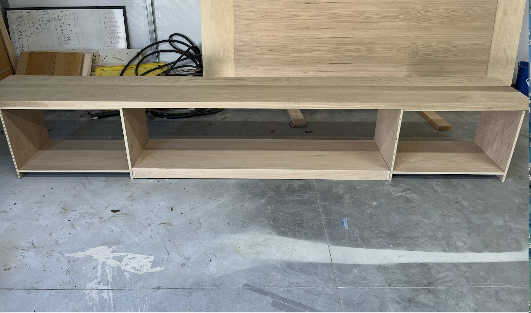 Wooden TV stand with open shelves on a concrete floor in a workshop.