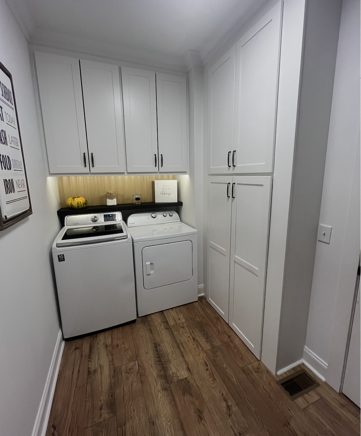 Laundry room with white washing machine and dryer, wooden cabinets, and a black countertop with small pumpkin and decorative items