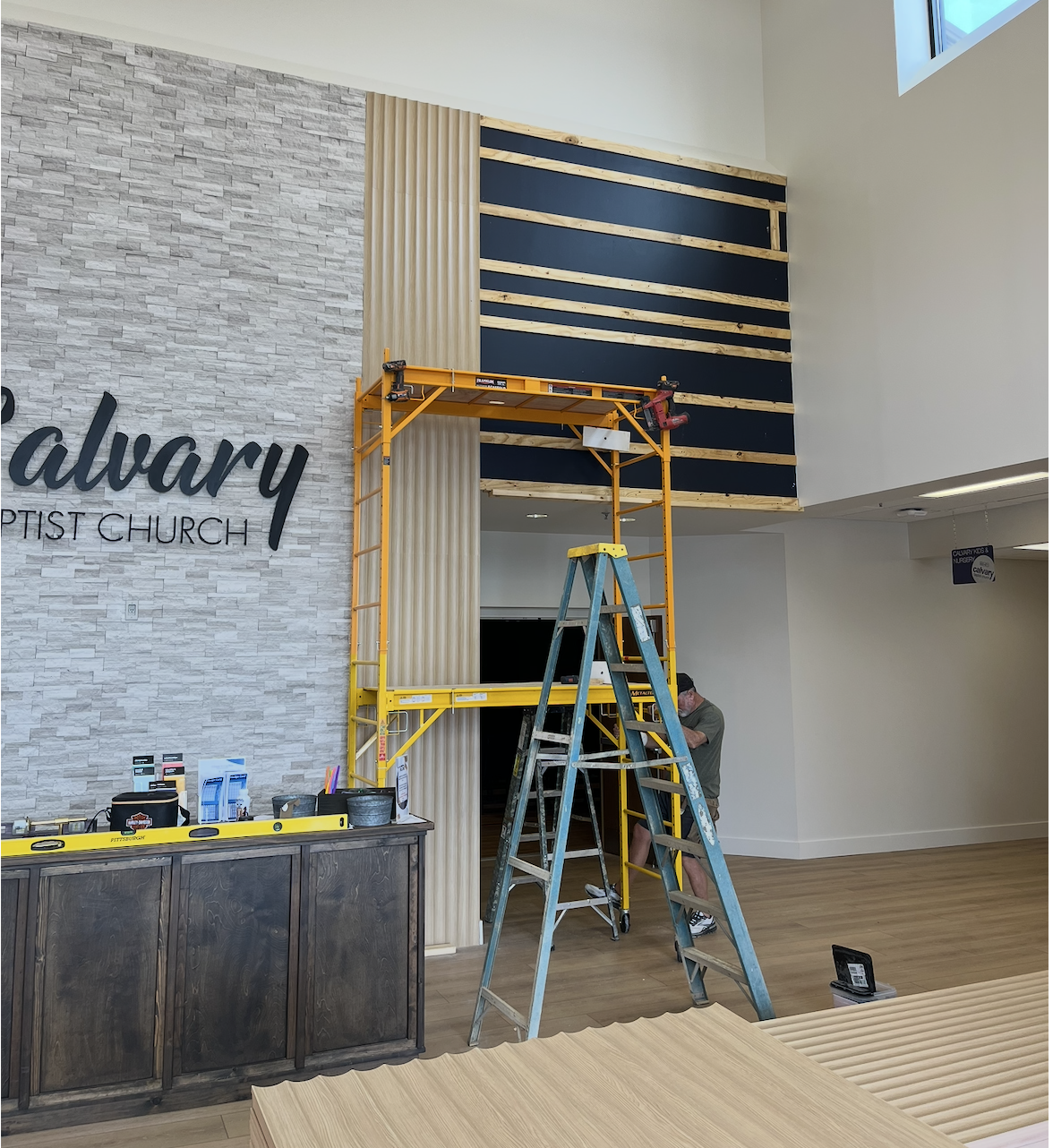 Construction worker installing wall panel near a church interior with a scaffold and ladder.