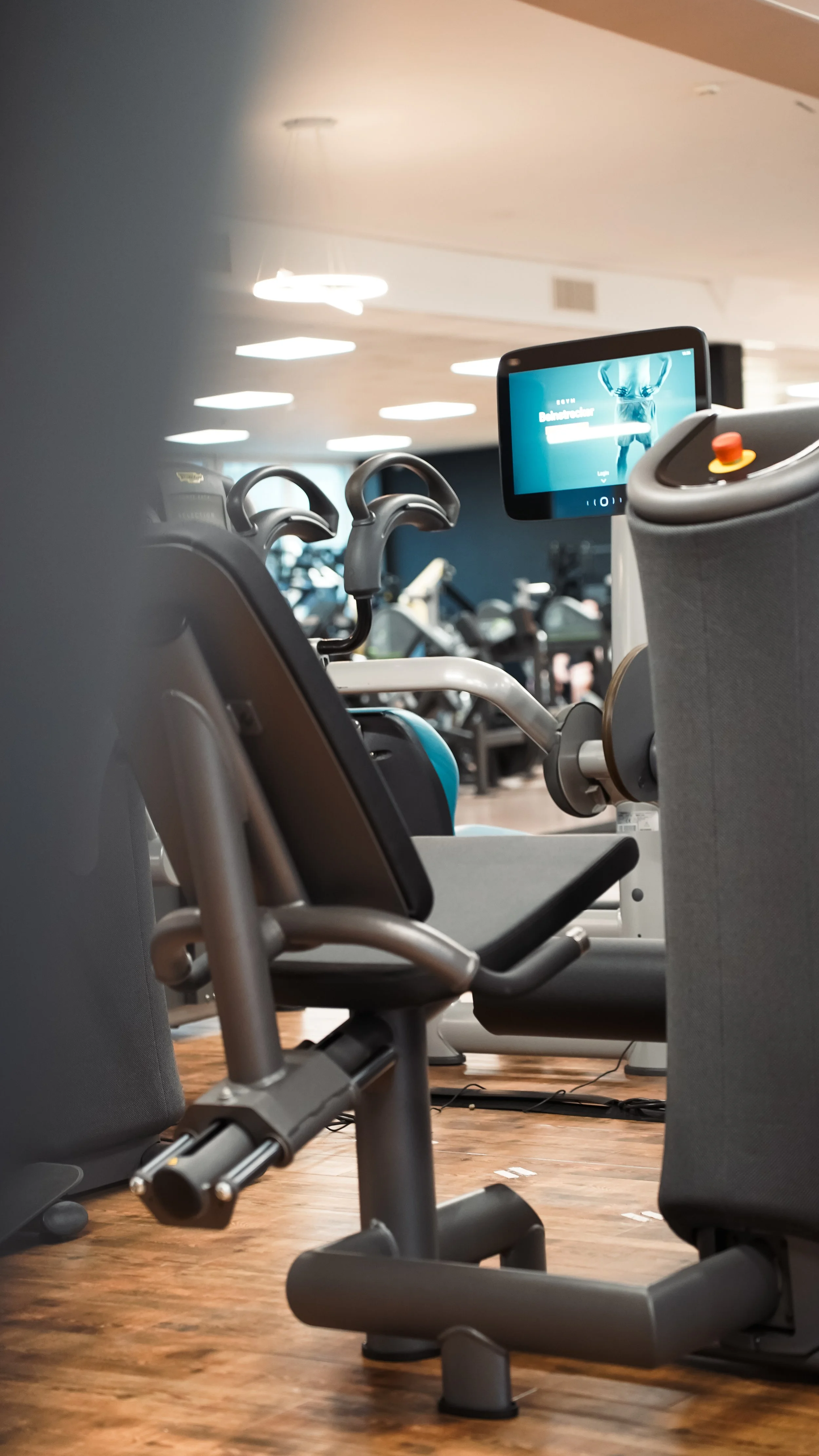 Leerer Fitnessraum mit modernen Trainingsgeräten, Kabelzugmaschine und Bildschirm-Displays.