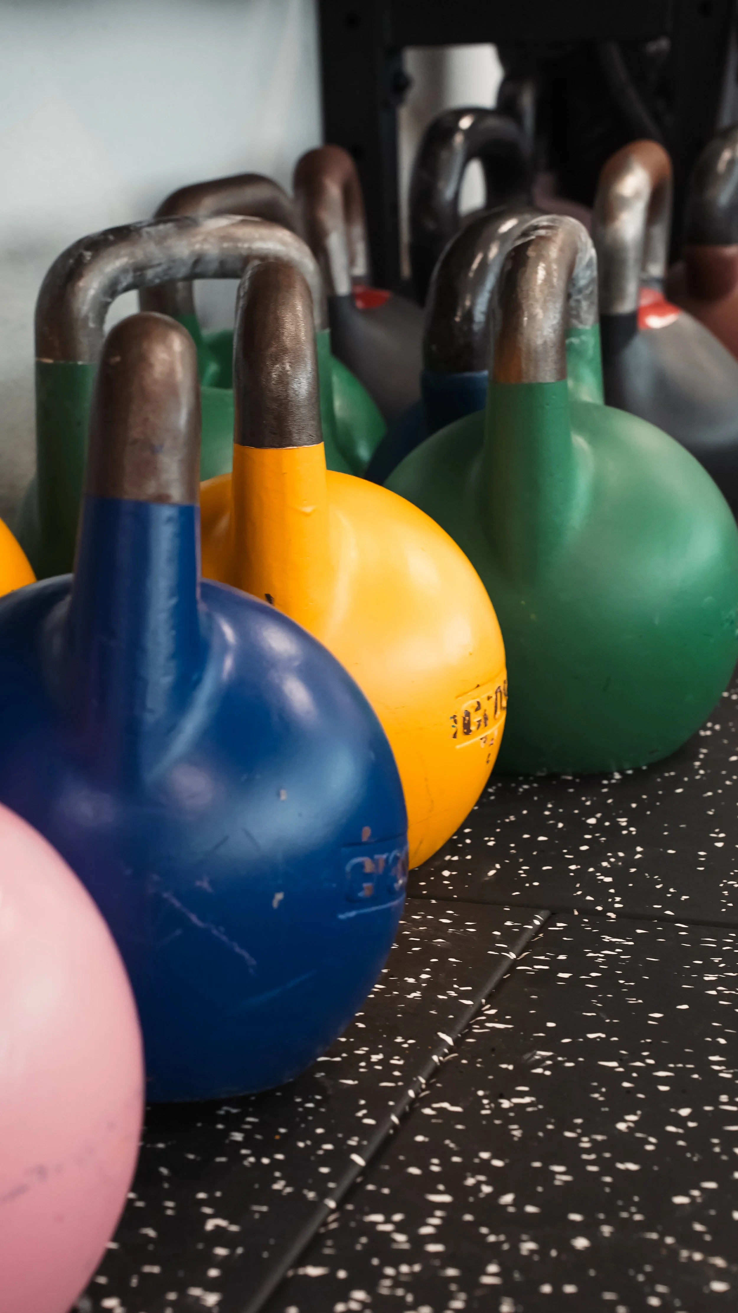 Mehrere farbige Kettlebell-Gewichte in Blau, Gelb, Grün und Schwarz auf einem schwarzen, gesprenkelten Boden