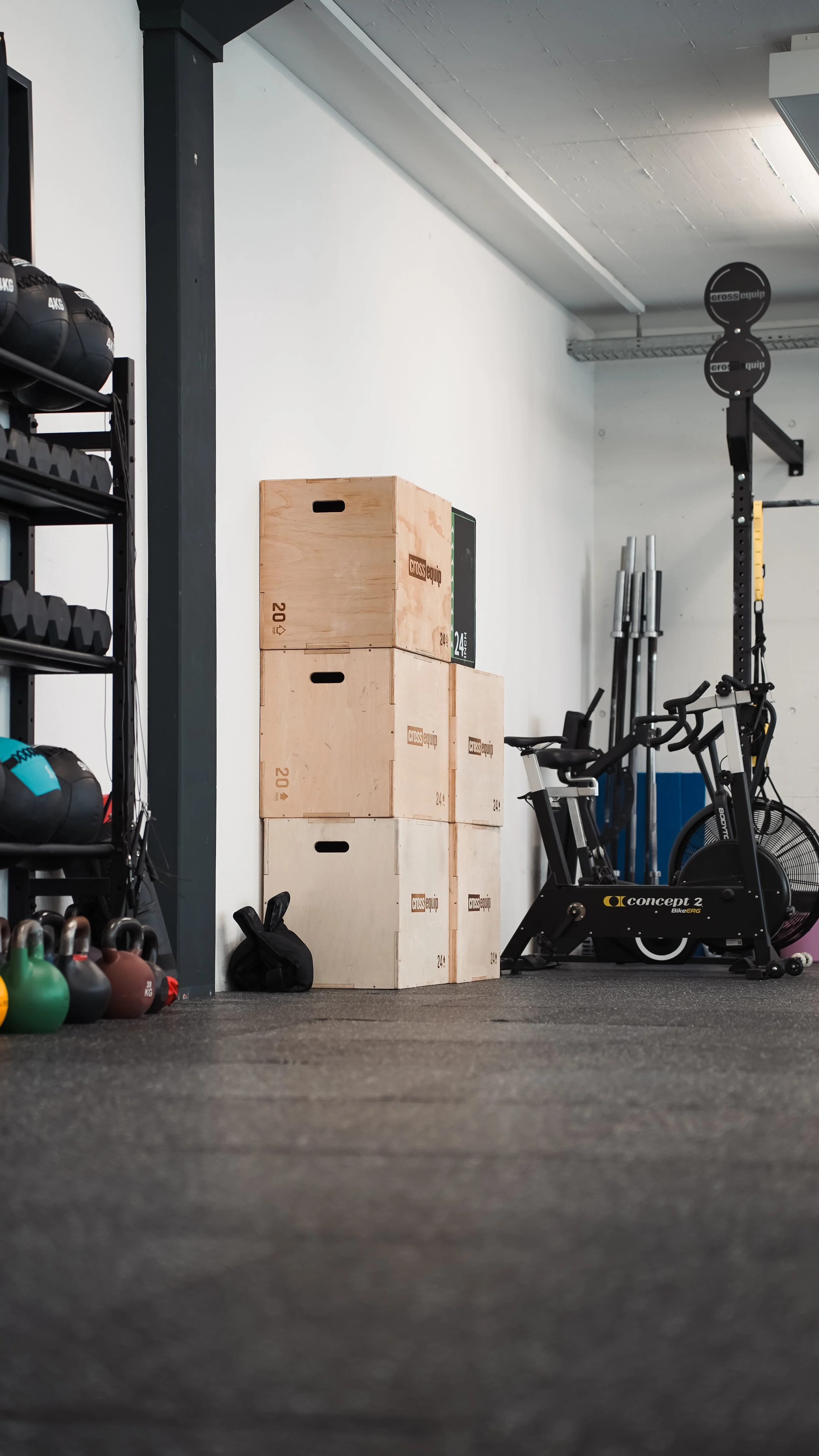 Kraftgeräte, Holzboxen, Fahrrad und Hanteln in einem Fitnessraum.