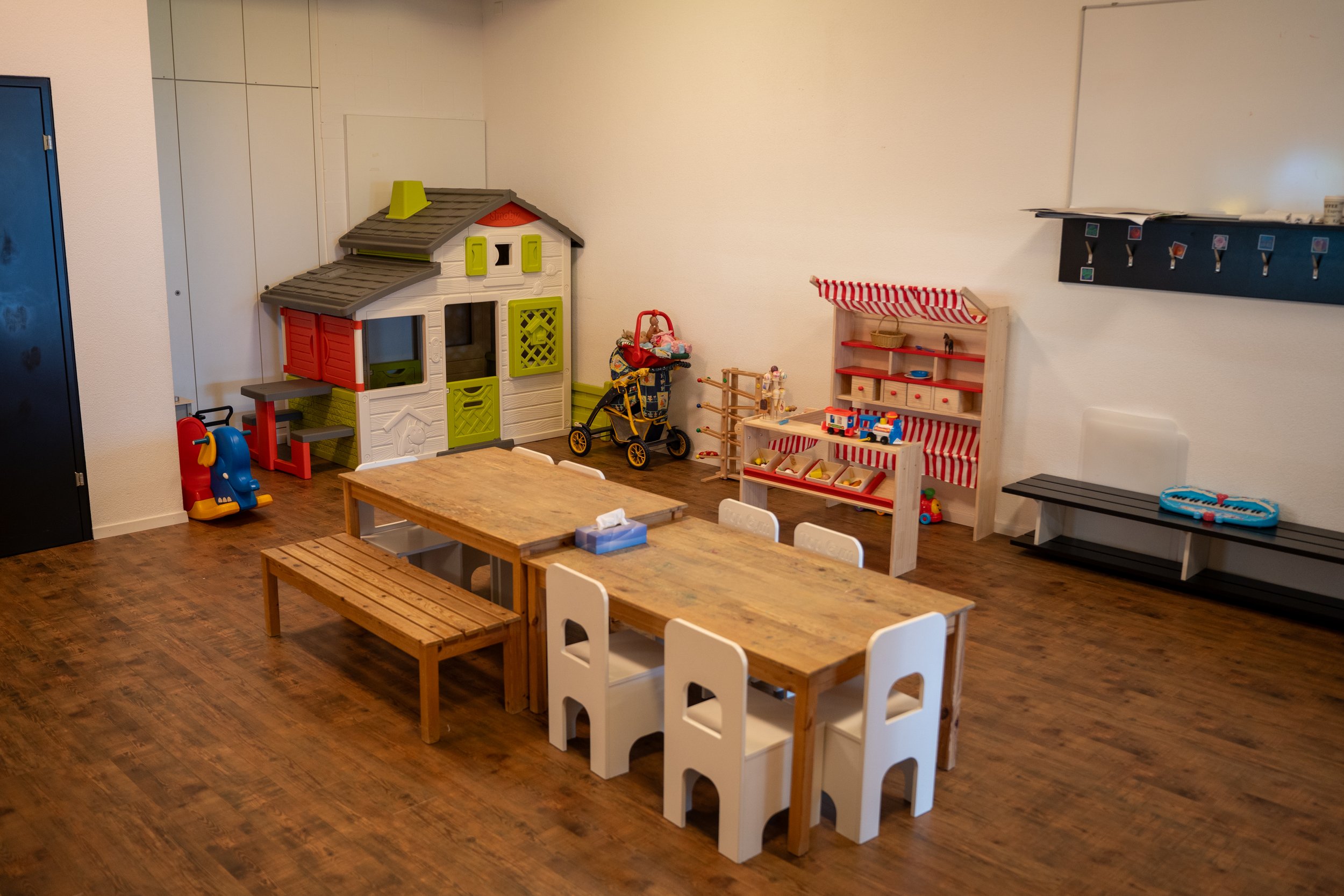 Spielzimmer für Kinder mit Holztischen, Kinderstühlen, Spielzeug, Spielhaus und Lernmaterialien