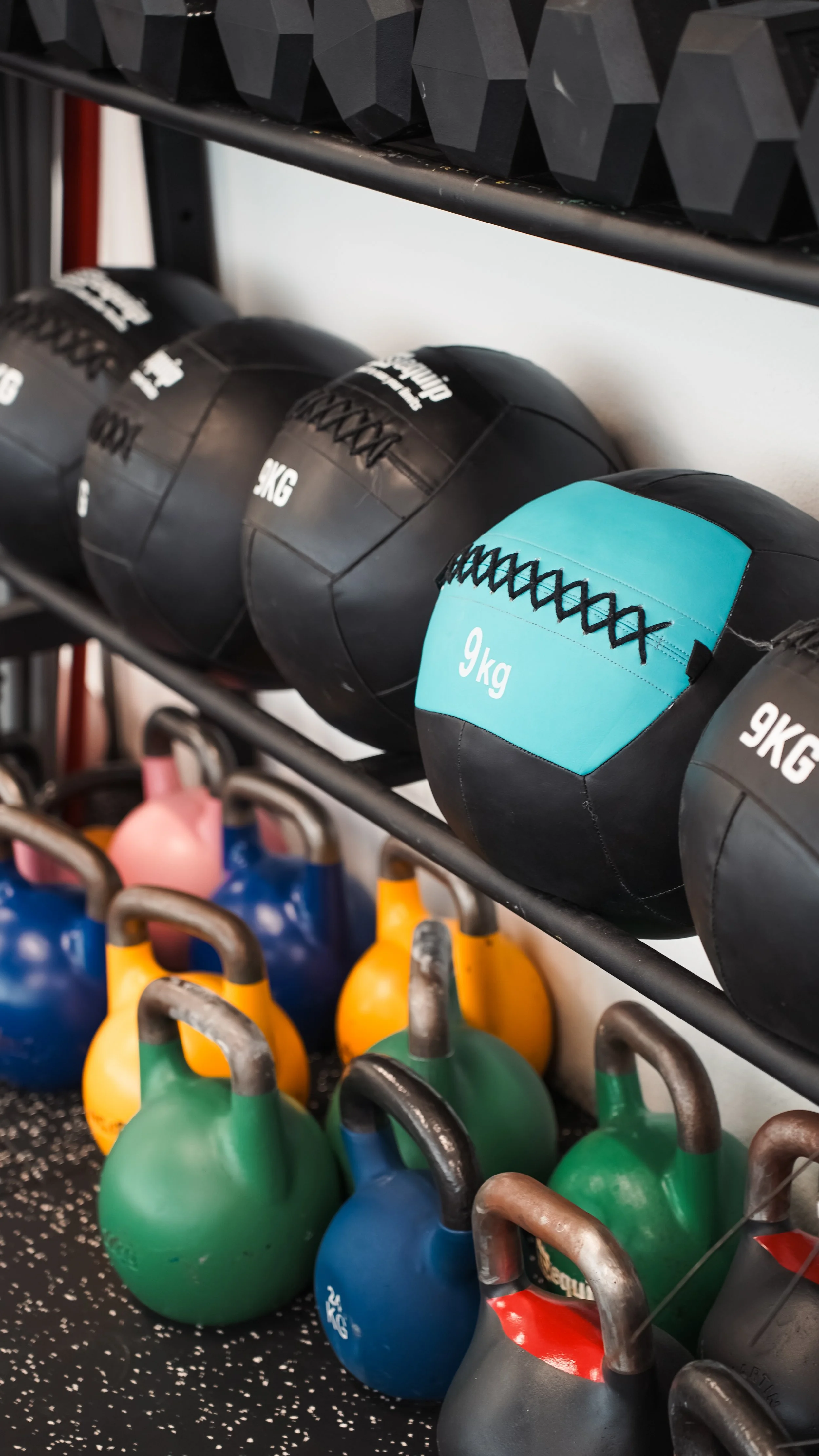 Schwere Medizinball mit 9 kg Gewicht auf einer Hantelablage, umgeben von bunten Kettlebells in einem Fitnessstudio.