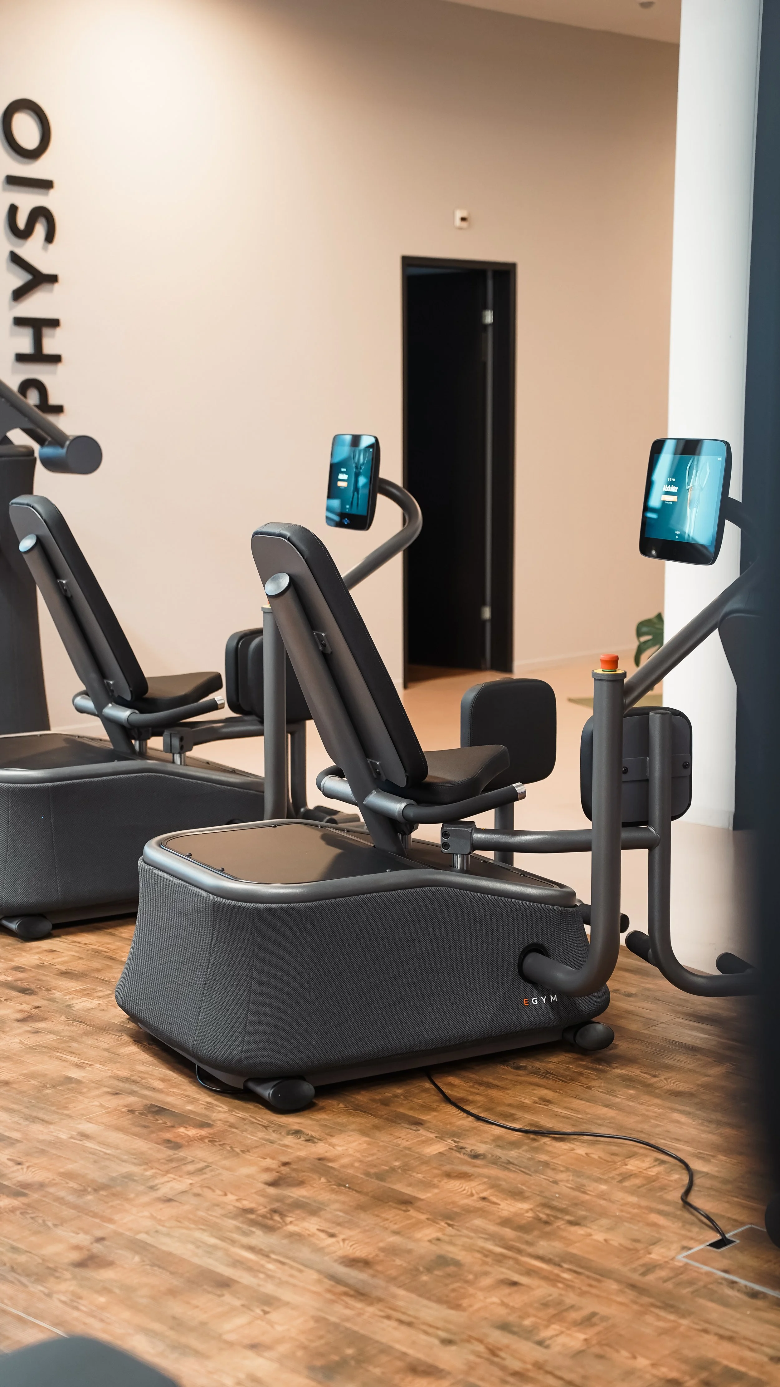 Zwei moderne vibrationstraining-Geräte mit Bildschirmen in einem Fitnessstudio, mit Holzfußboden und weißen Wänden.