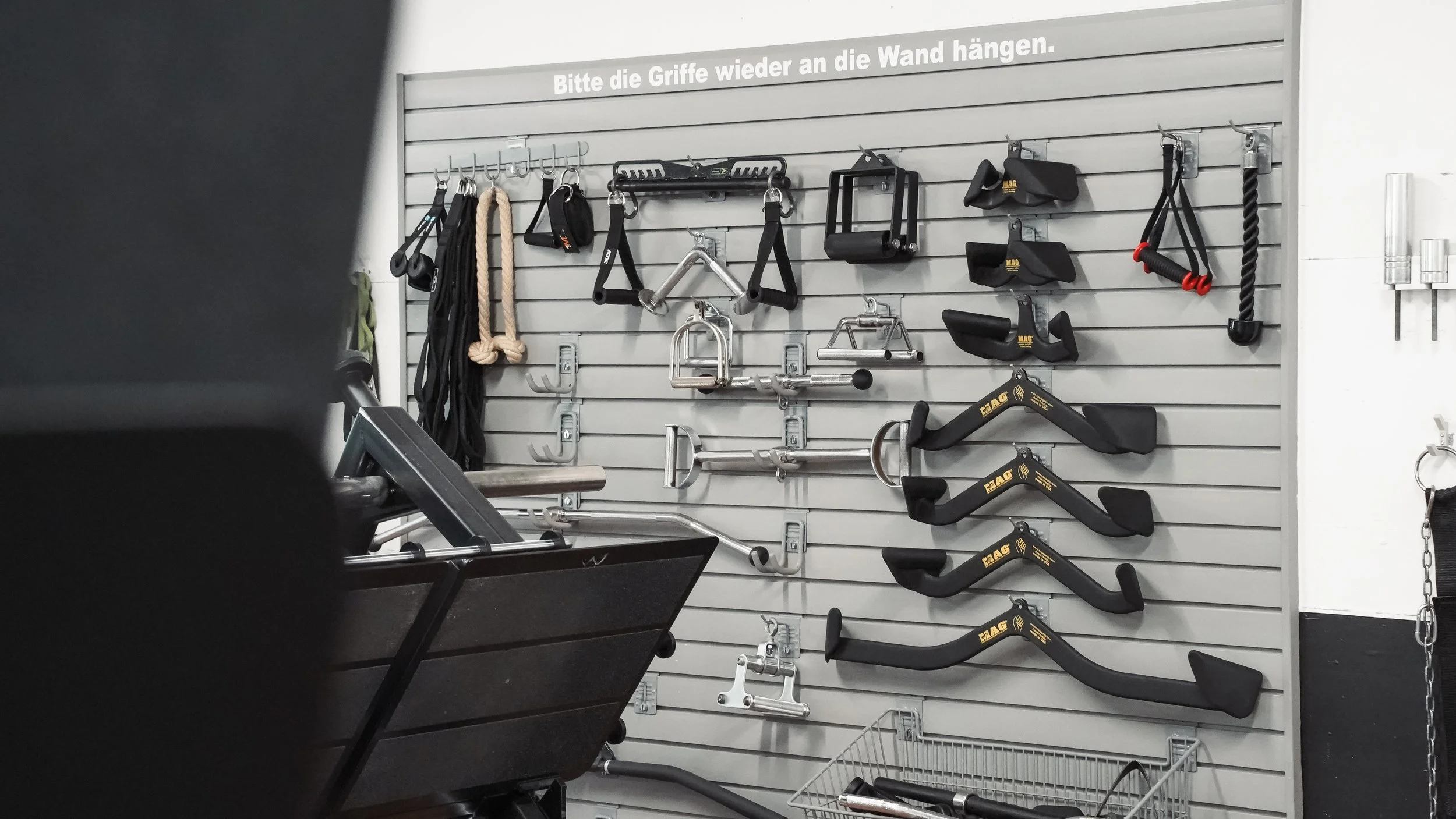 Hantelstangen, Klimmzugstangen, Ringe, Seilzüge und Trainingshaken an einer Wand in einem Fitnessstudio.
