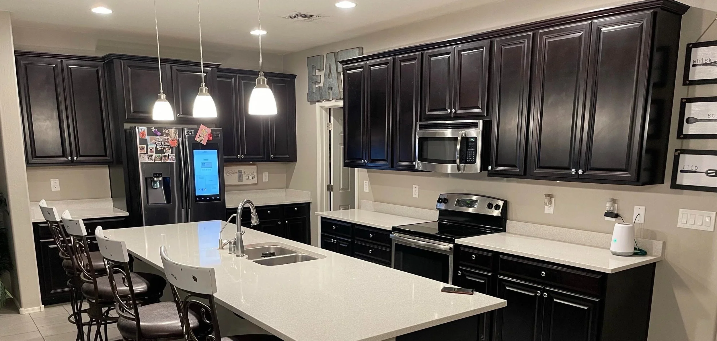 Modern kitchen with black cabinets, white countertops, stainless steel appliances, and a large island with barstools.