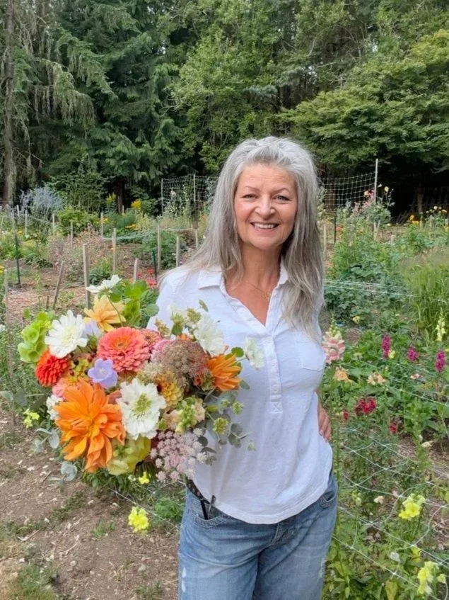 woman holding Vibrant dahlia bouquet floating above rows of colorful zinnias and dahlias in a farm field.