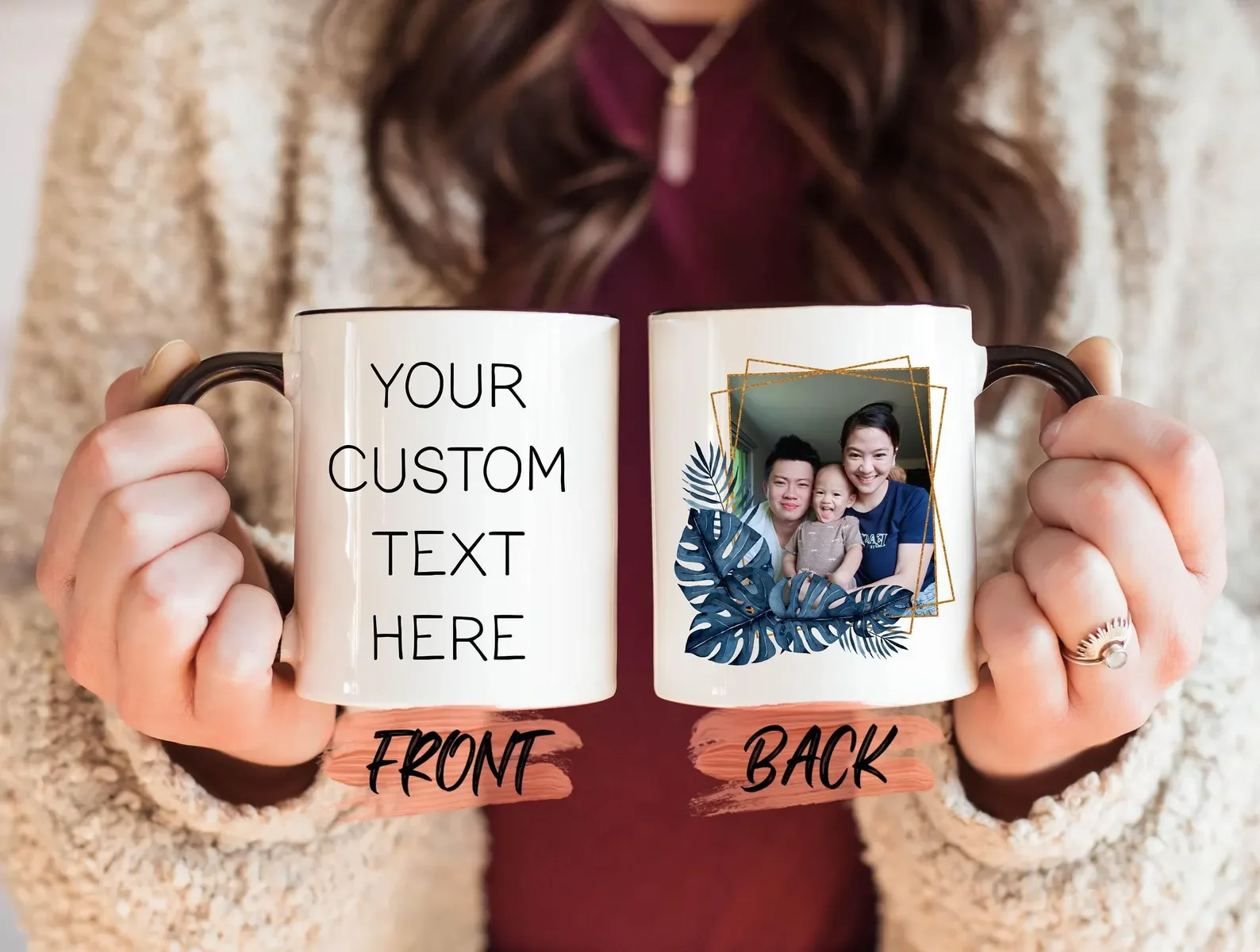 Person holding two ceramic mugs, front mug has customizable text, back mug features a photo of a family with a woman, a man, and a young child, surrounded by leafy tropical design.