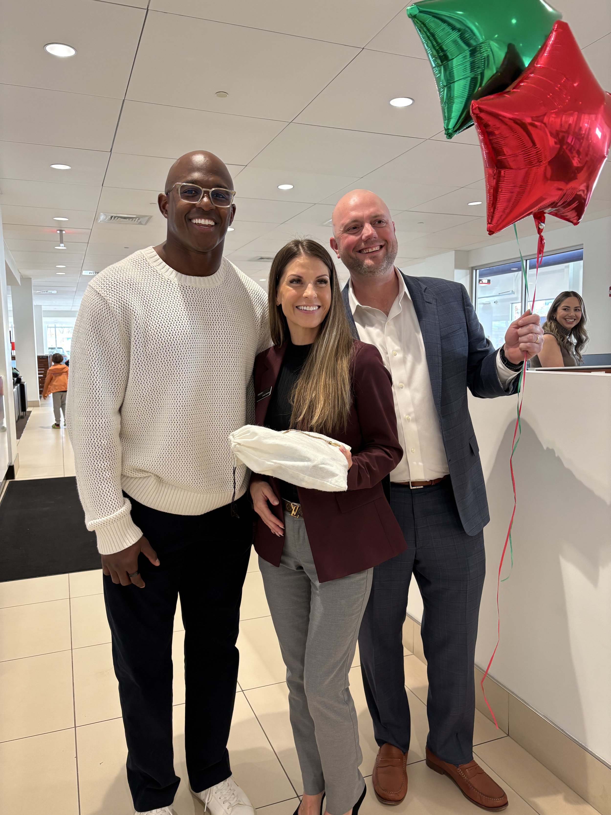 NFL new england patriots michael slater at group 1 auto in boston smiling adults standing together indoors, with balloons, celebrating a special occasion.
