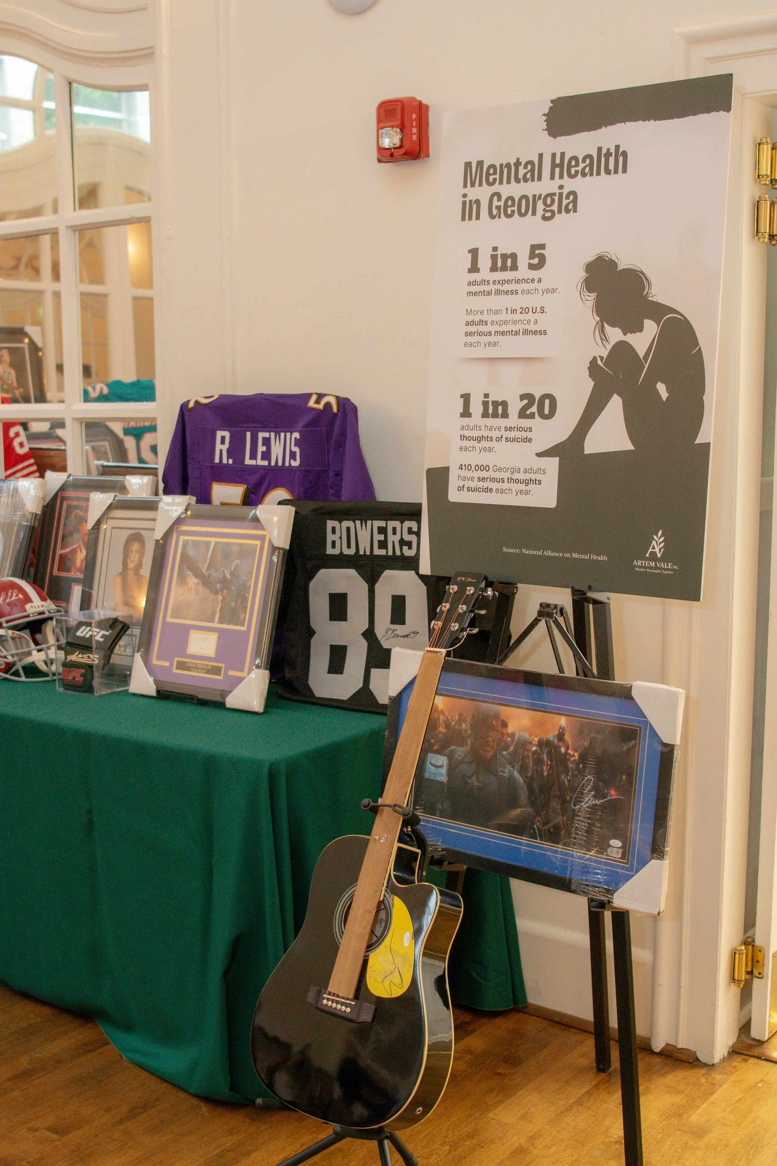 Display table with framed photographs, sports jerseys, a guitar, and a poster about mental health in Georgia, showing statistics about mental illness and suicidal thoughts.