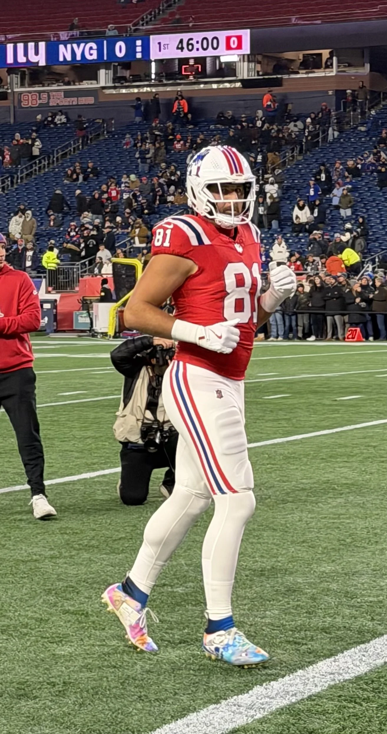 A football player in a red uniform with number 81, wearing a white helmet and colorful running shoes, standing on a football field during a game.