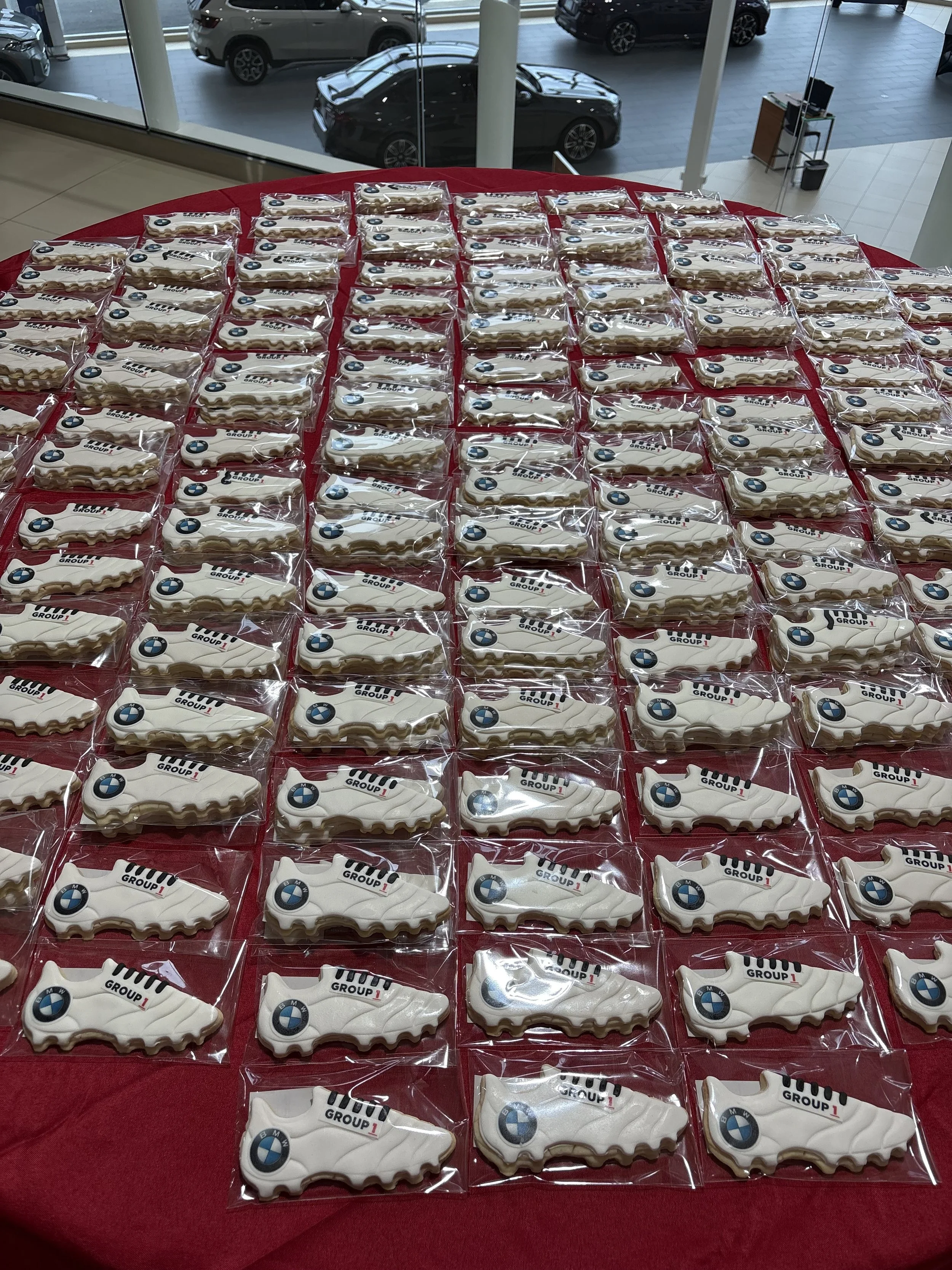 Cookies with BMW logo and 'GROUP 1' printed on them, arranged on a red tablecloth in a dealership or event space.