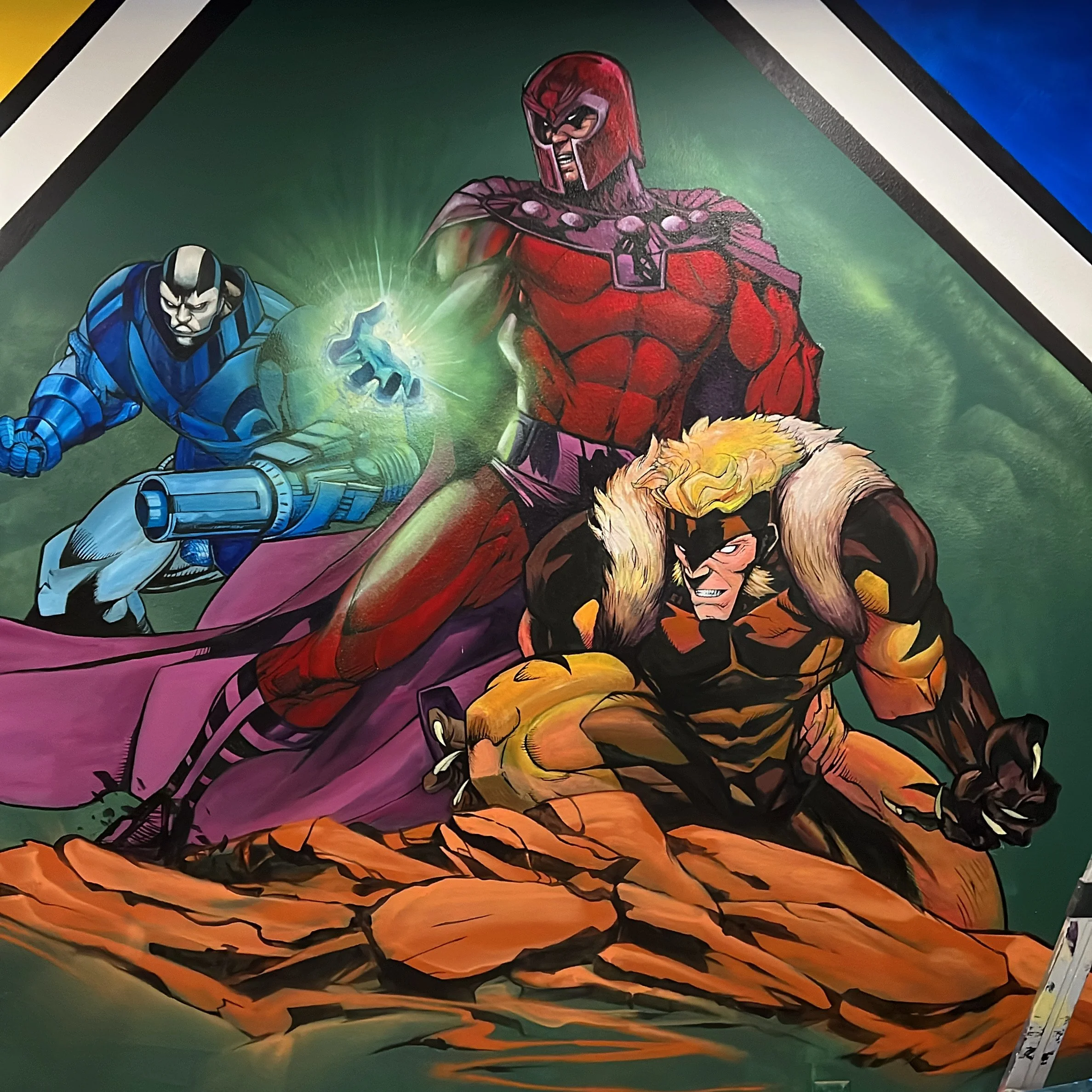 Comic book-style illustration of three superheroes in dynamic poses, standing on cracked rocks with a green background. The central figure is a muscular man in a red costume with a helmet, purple cape, and a glowing green energy in his hand. To his l