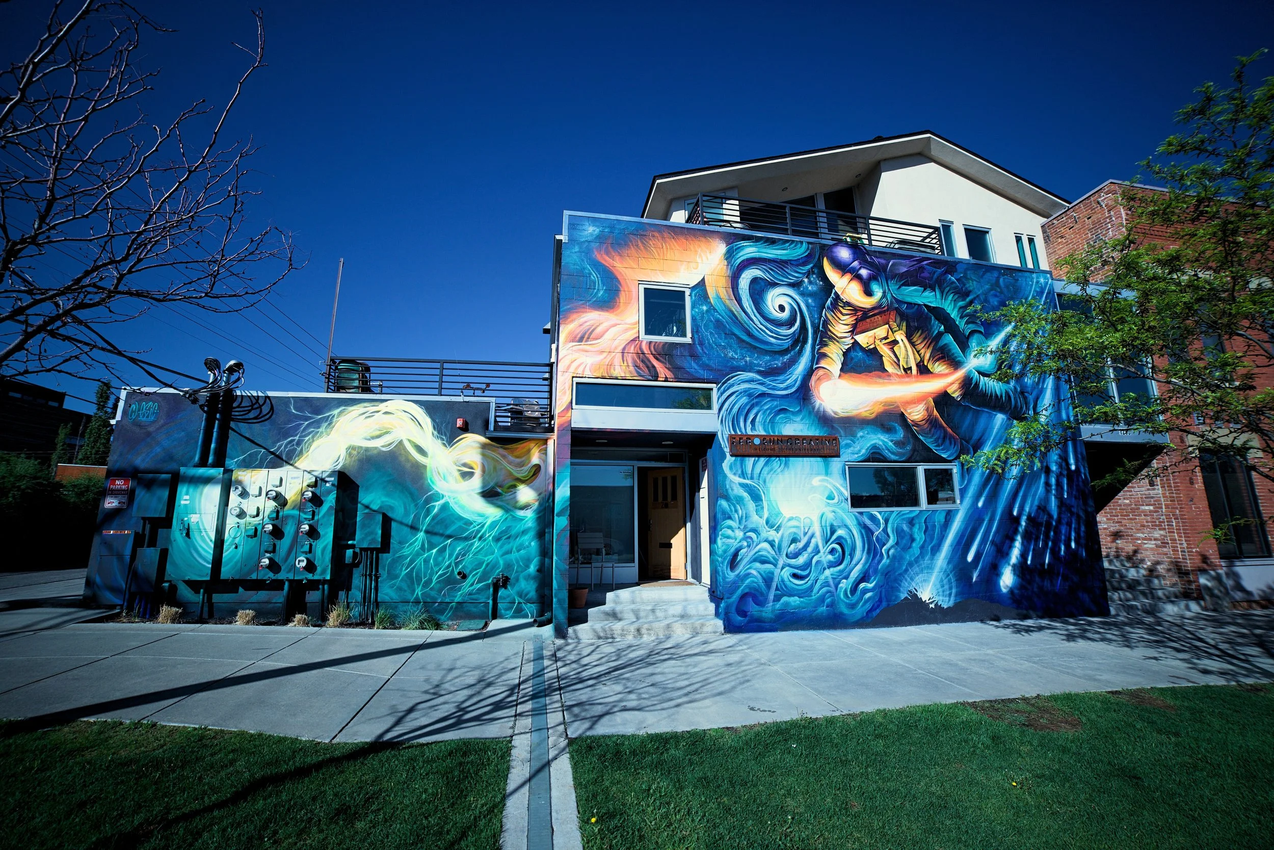 Colorful mural on building wall depicting a person in astronaut suit referencing Van Gogh's Starry Night with swirling patterns, flames, and cosmic elements.